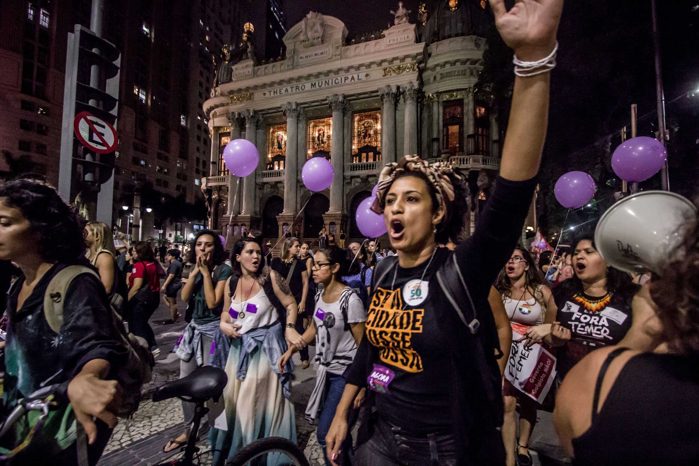 Women march in a protest in the downtown. They chanting as they are walk, wearing protest phrases and signs.