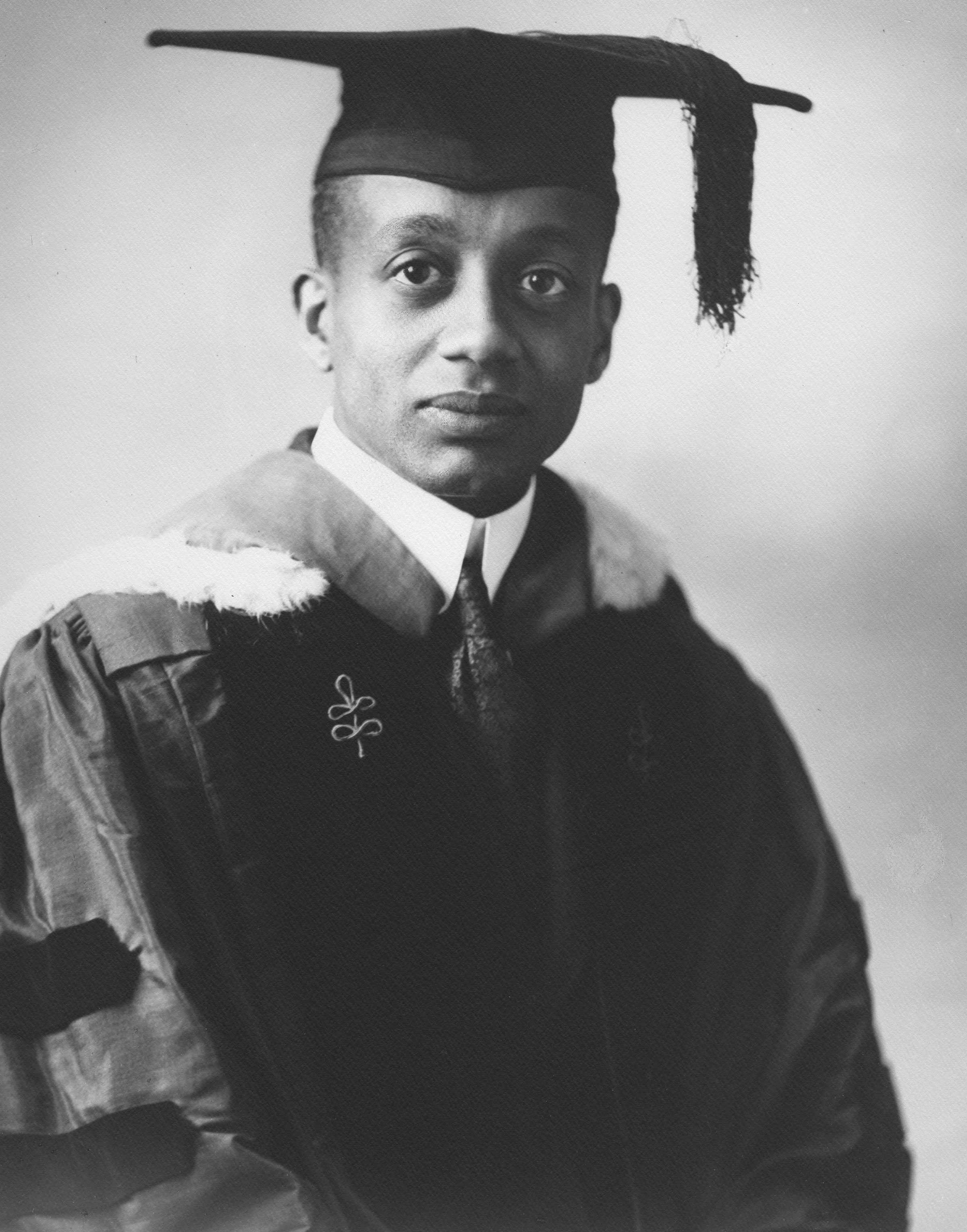 Black and white portrait of an African American man in academic regalia including a cap and gown.