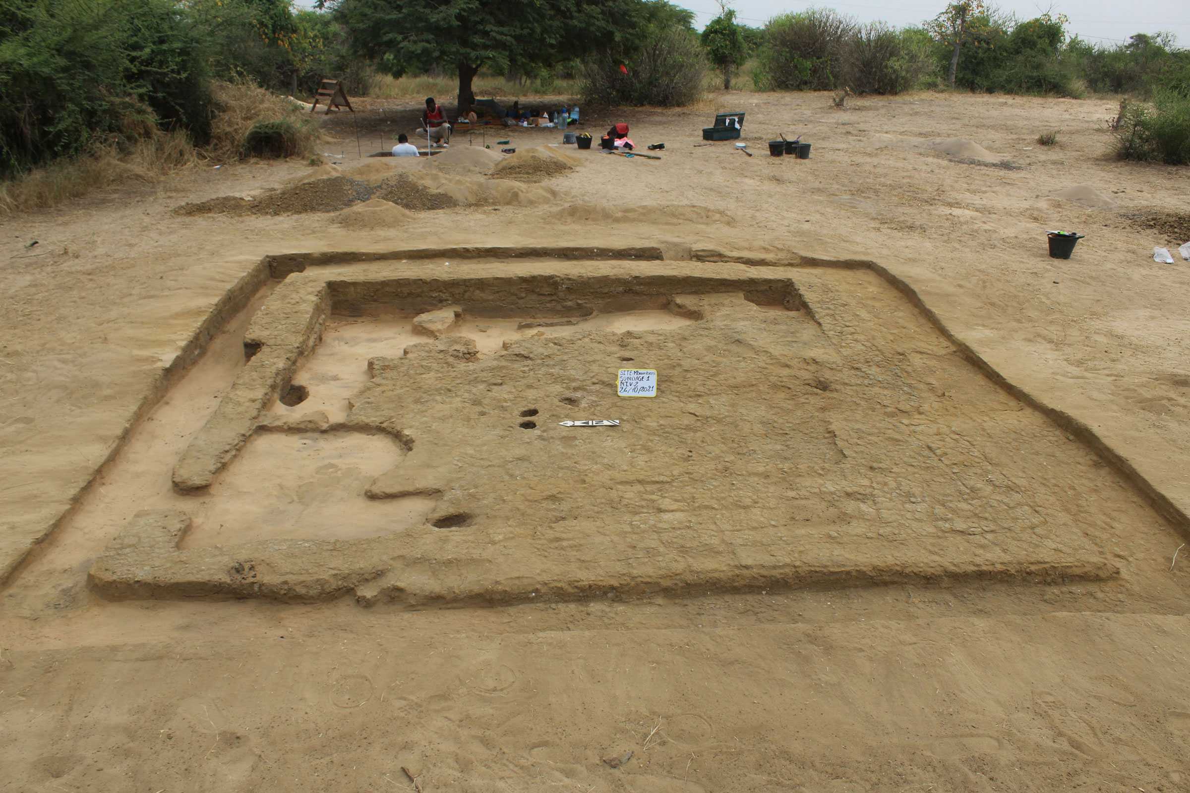 A square excavation of Marème Diarra’s dwelling in sand. A single shallow wall towards the back.