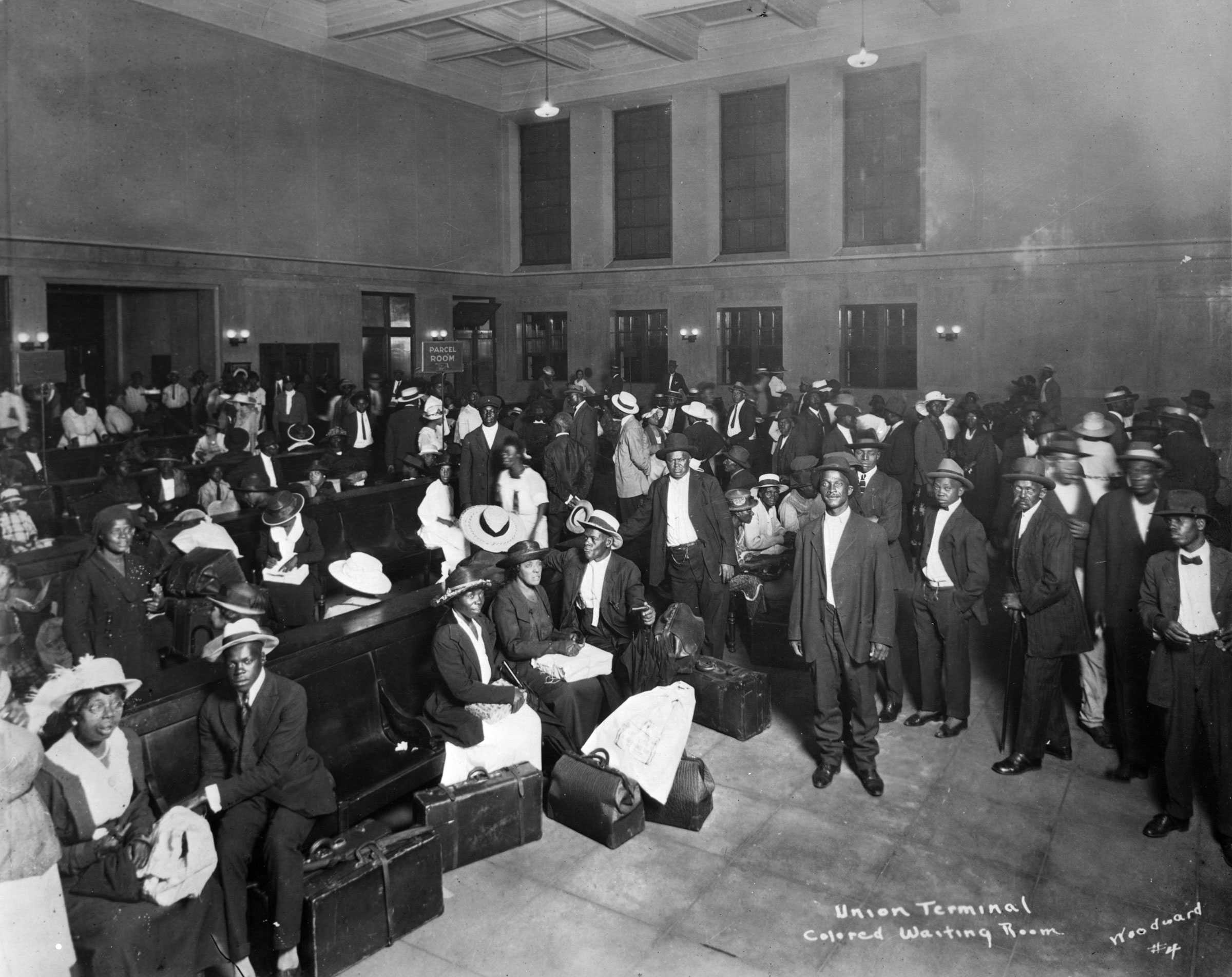 Black and white photograph of African Americans seated and standing in a waiting room.  There is writing on the photograph that identifies it "Union Terminal / Colored Waiting Room."