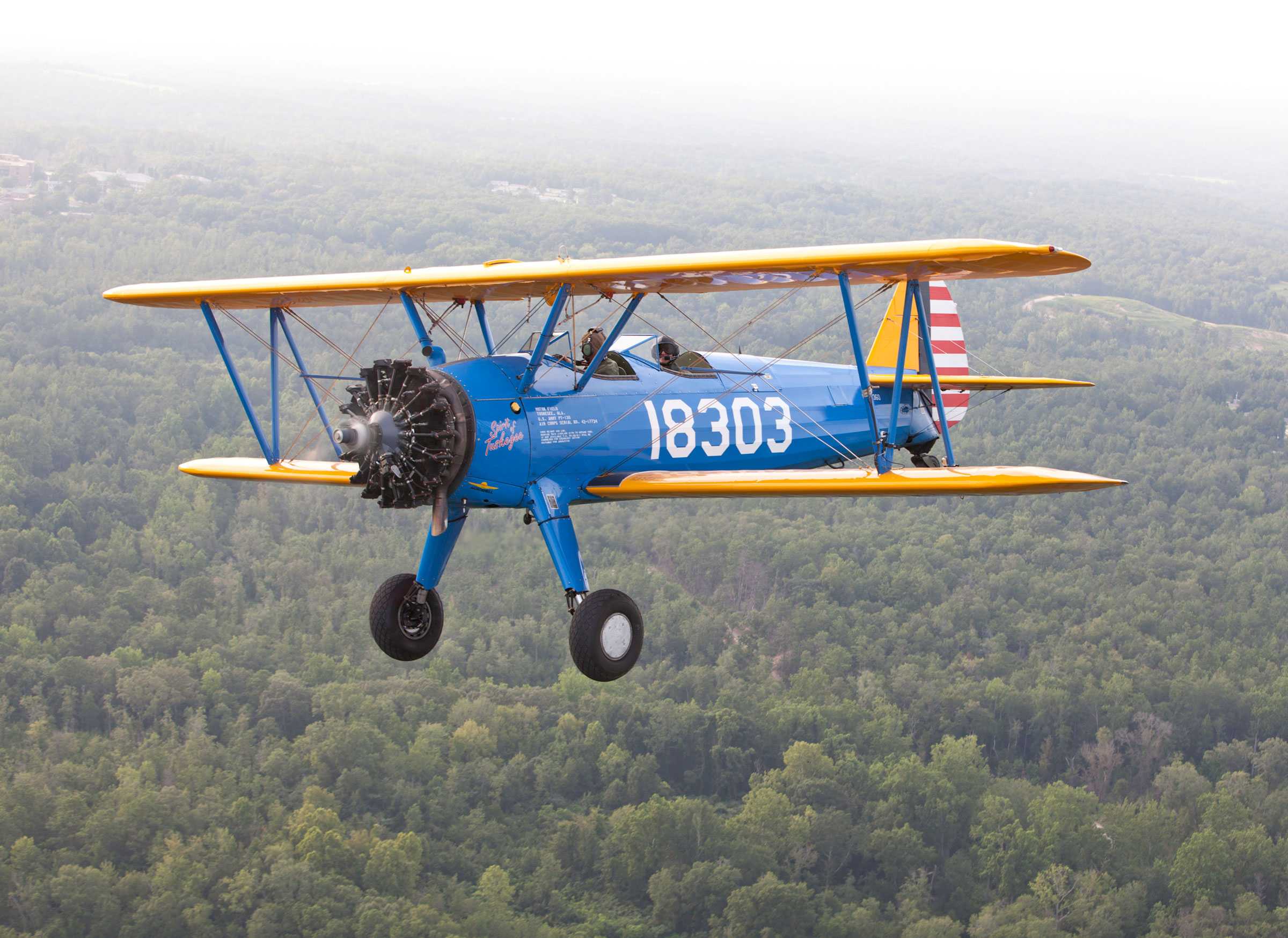 The PT-13D Stearman Kaydet has a blue body, yellow wings, and "Spirit of Tuskegee" in red on the cowl.