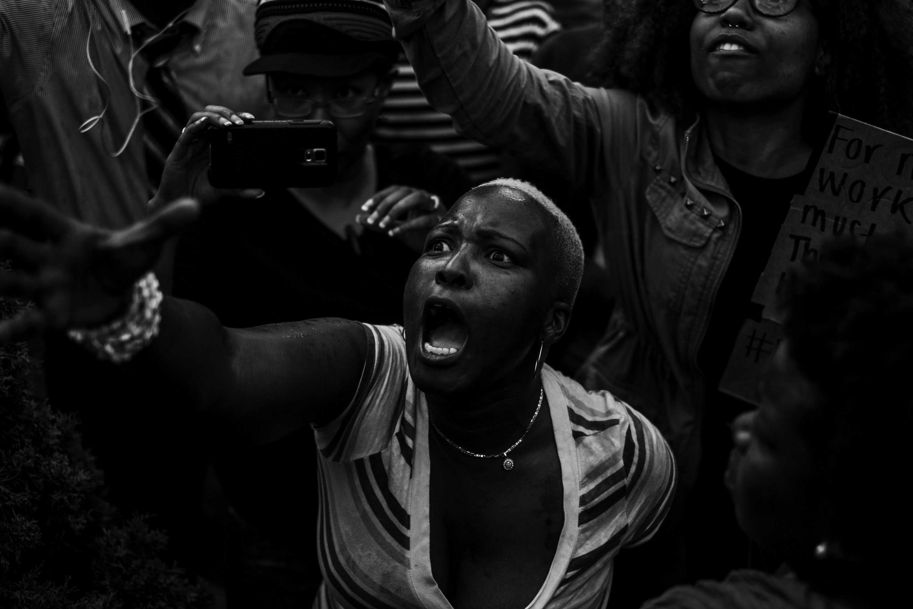 A Black-and-white photo of a women protesting with her right arm reaching upward and her hand outstretched.