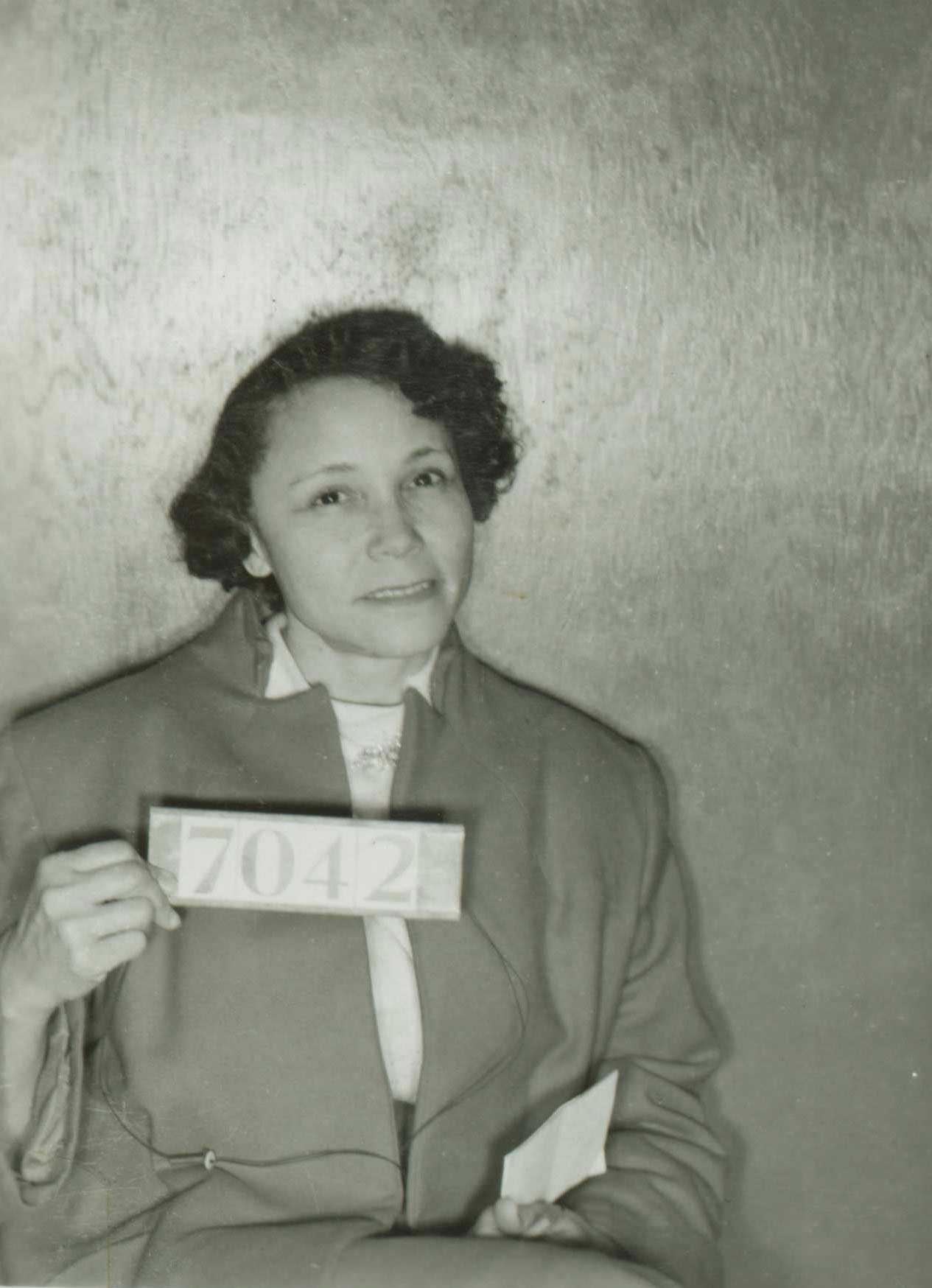 A black and white mug shot of Jo Ann Robinson. She smiles hesitantly while holding her inmate number.