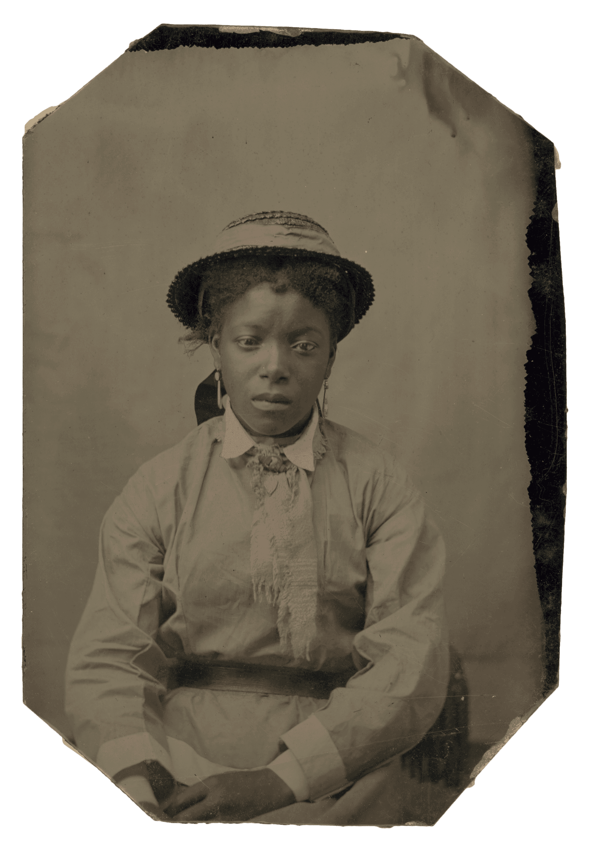 A tintype of an unidentified African American woman in a hat, earrings, and dress with painted pink cheeks.