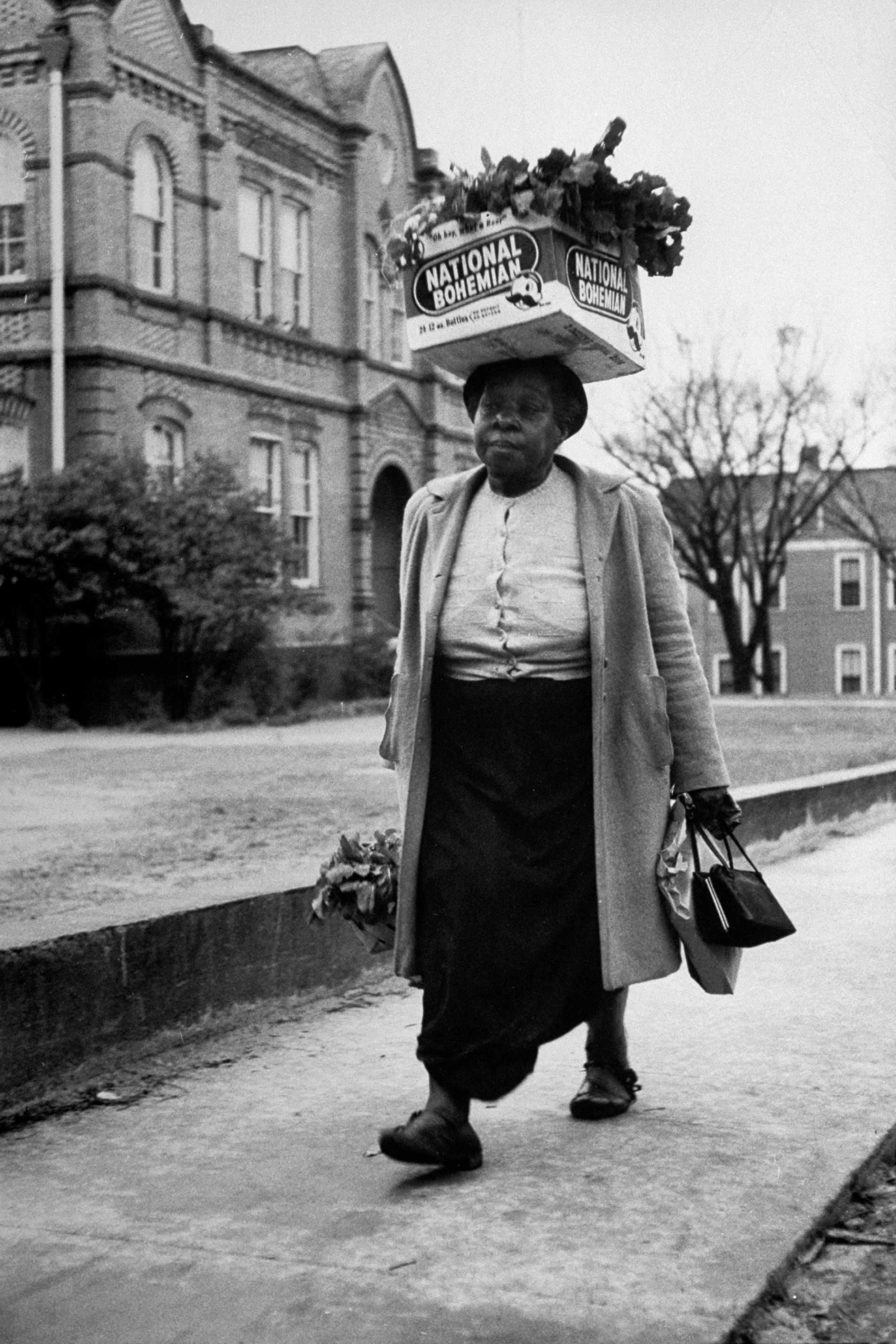 A older woman walking with box of turnip greens on her head during the Montgomery Bus Boycott.