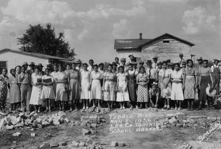 A group of women stand together outside the vocational training school. The photograph has a handwritten name and date of the school.