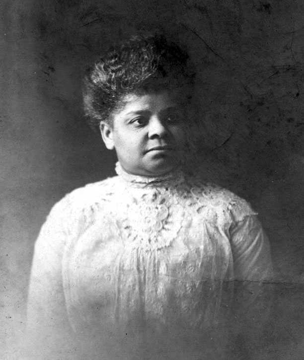 Black and white photograph of an African American woman.  She is dressed in a white lace and eyelet dress.