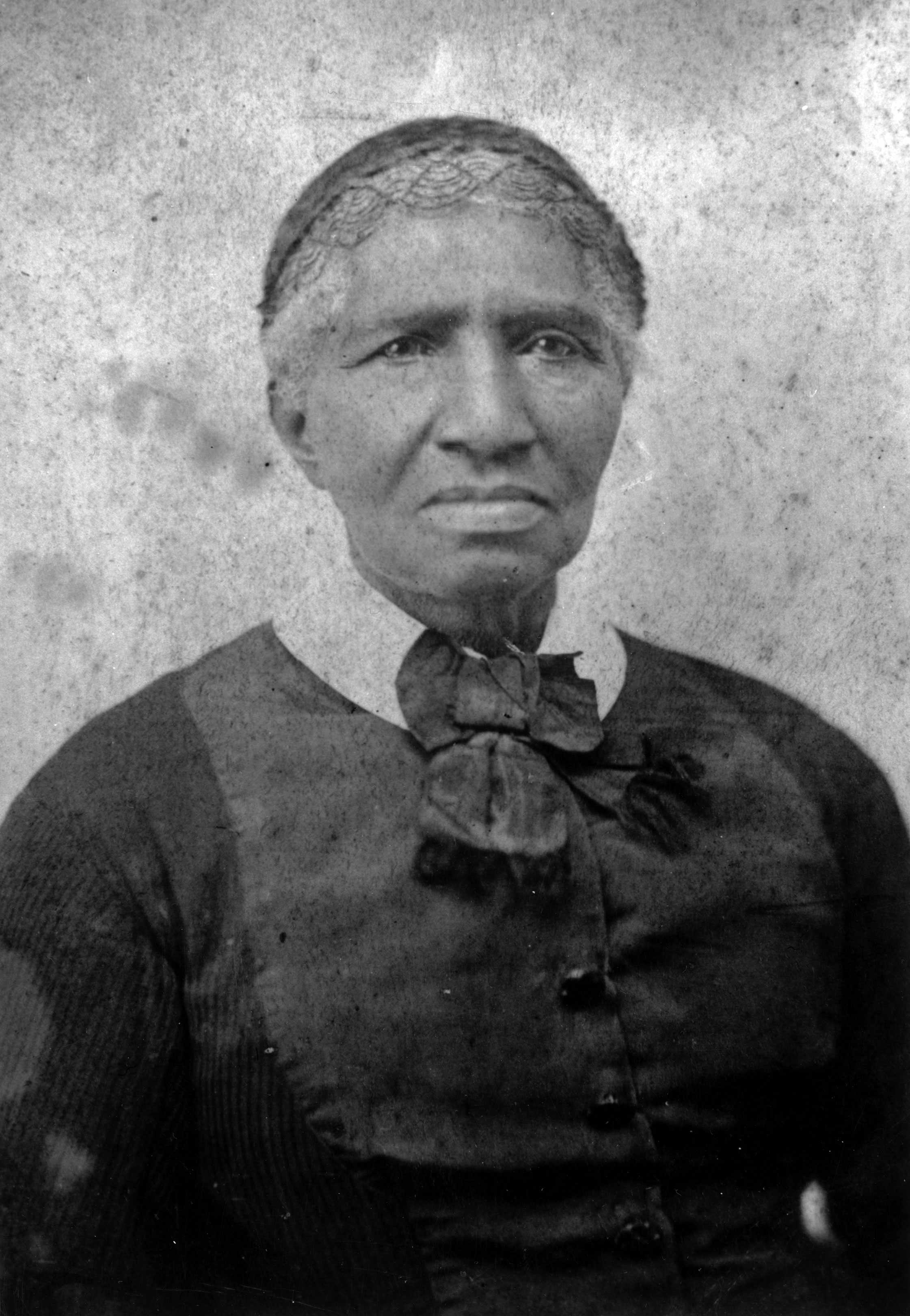 A cloudy black and white photograph of Clara Brown posing for a portrait. She is dressed in most black.