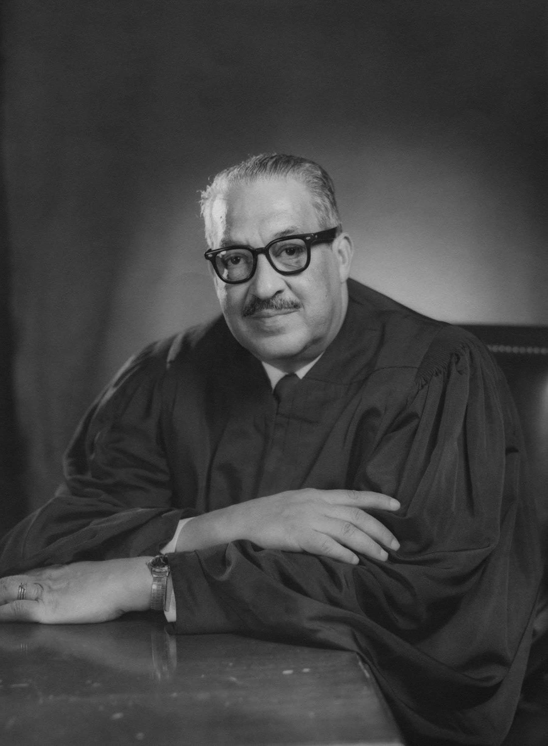 A black and white official portrait of Justice Thurgood Marshall. He is wearing dark rimmed glass and judges robe.