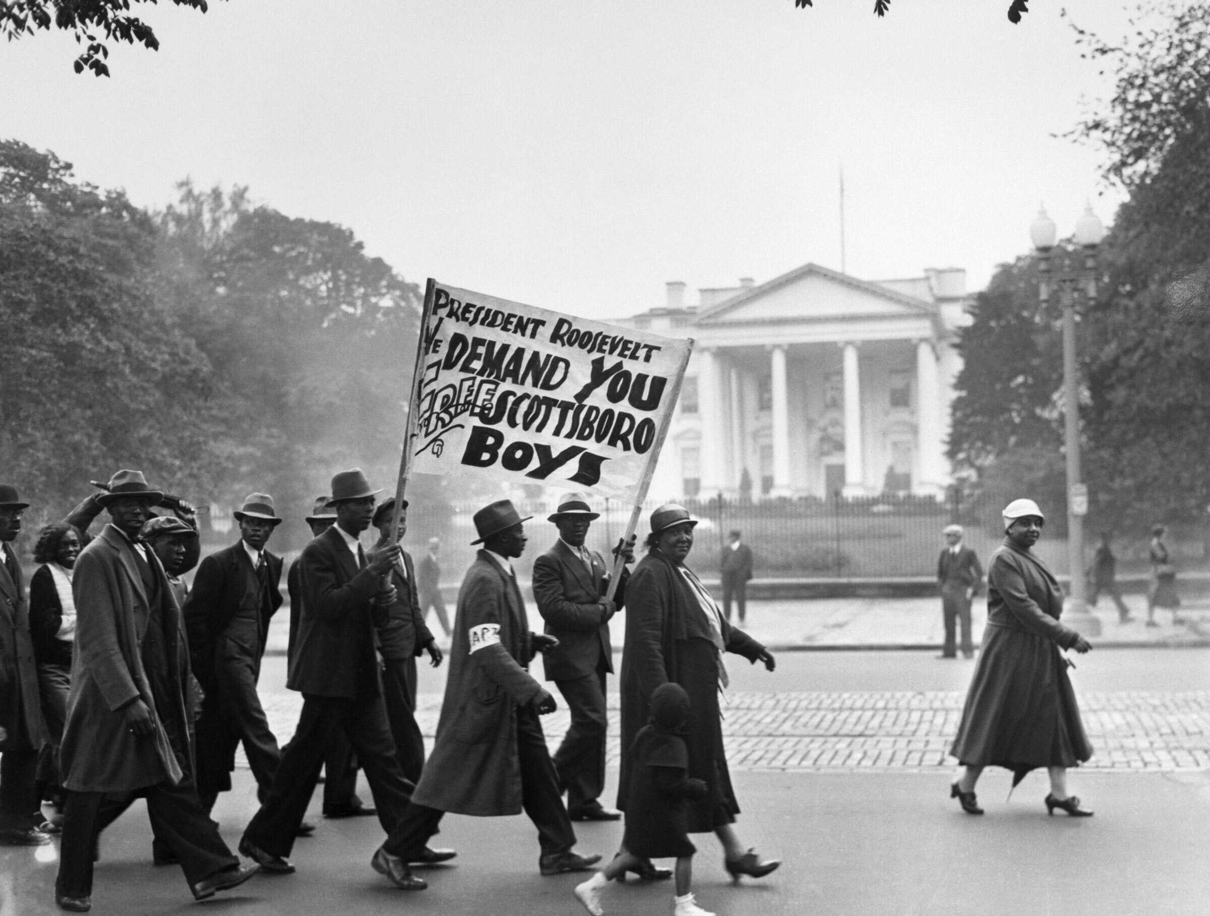 A black and white photograph of group of protestors walking in front of the White house.