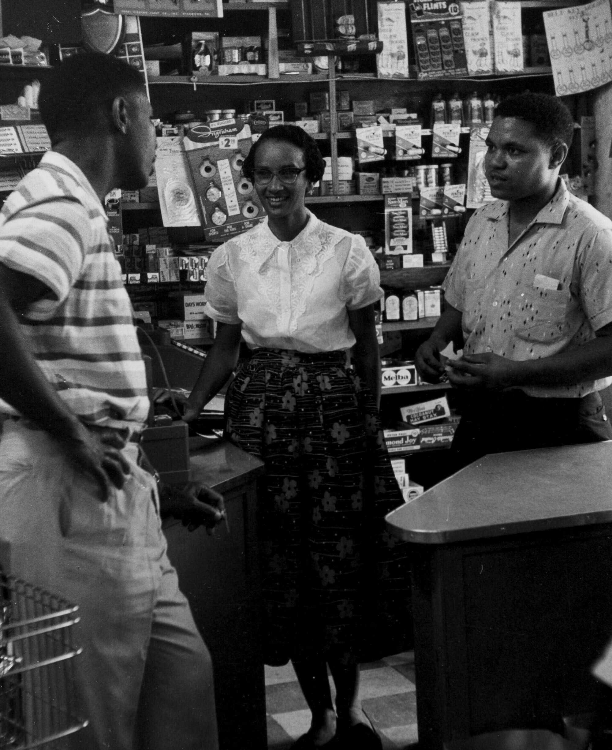 Black and white photograph of Medgar Evers speaking with a man and a woman in a grocery store.