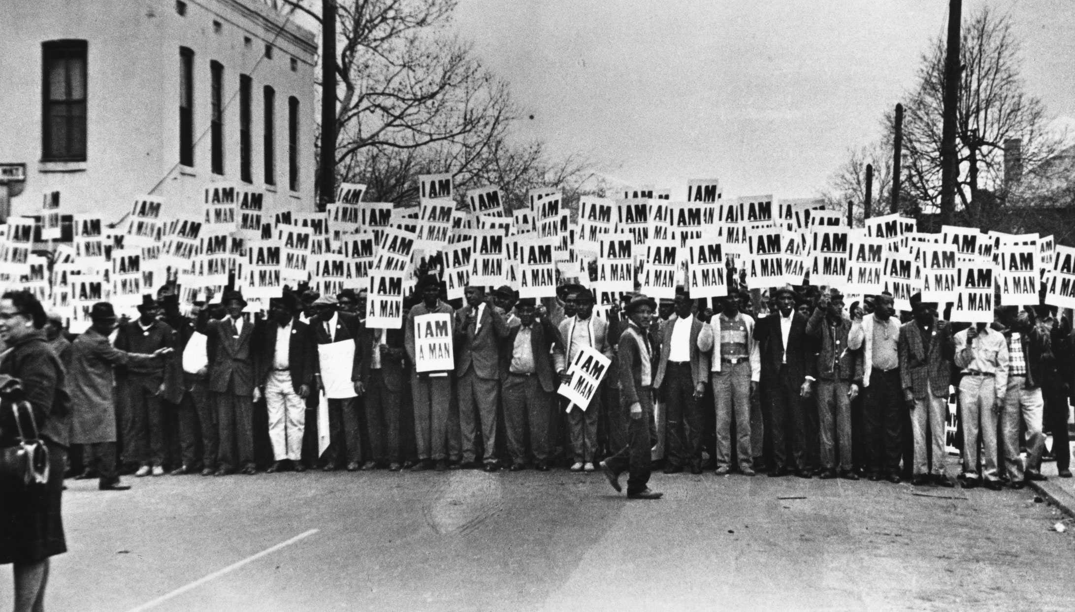 A black and white photograph of a group of male workers in formation on the street holding signs that read "I Am A Man."