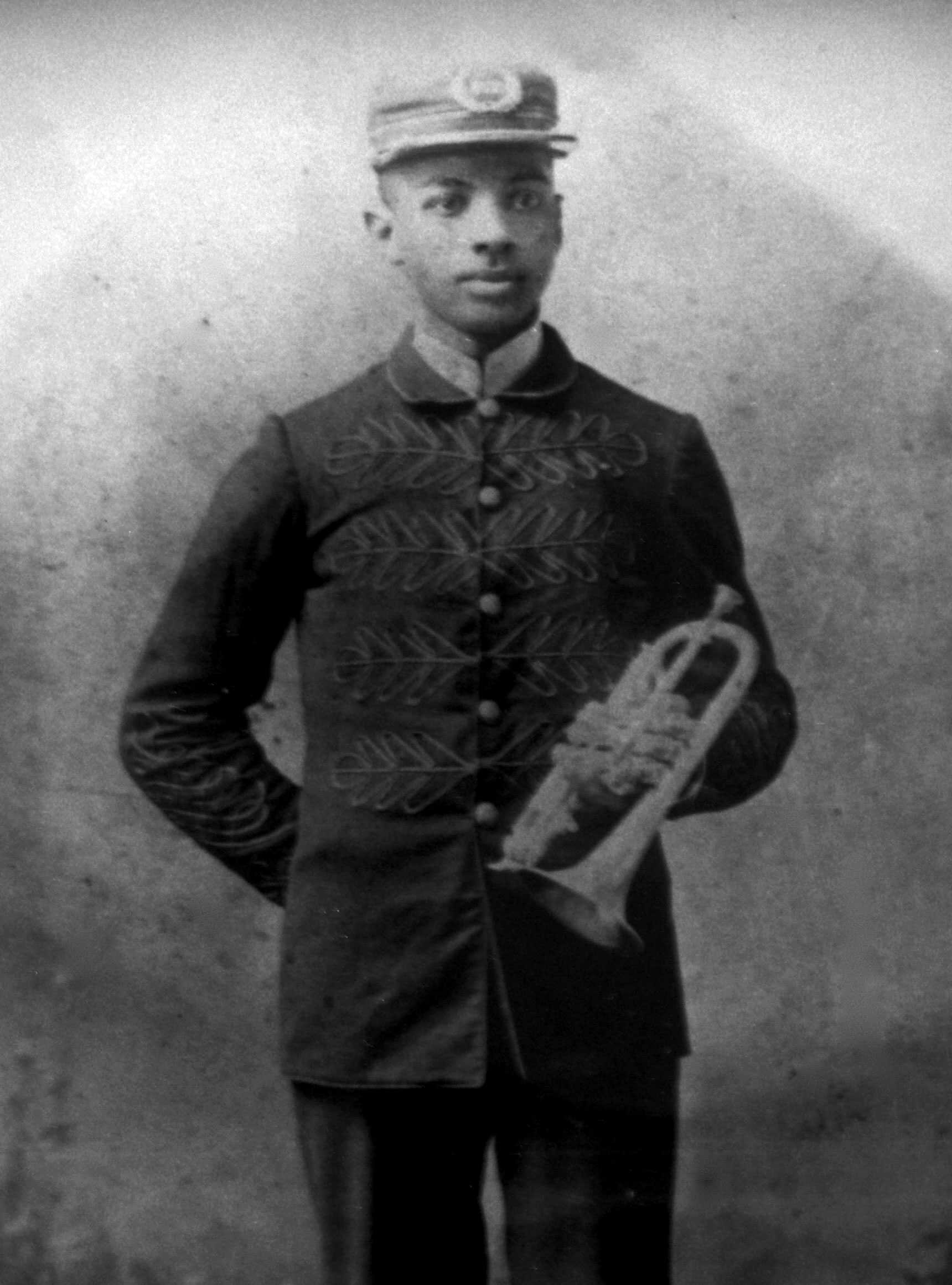 Portrait of a young black man holding a trumpet.  He is wearing a decorative jacket and cap.  The subject is identified below the image as " W.C. Handy / (age 19)."