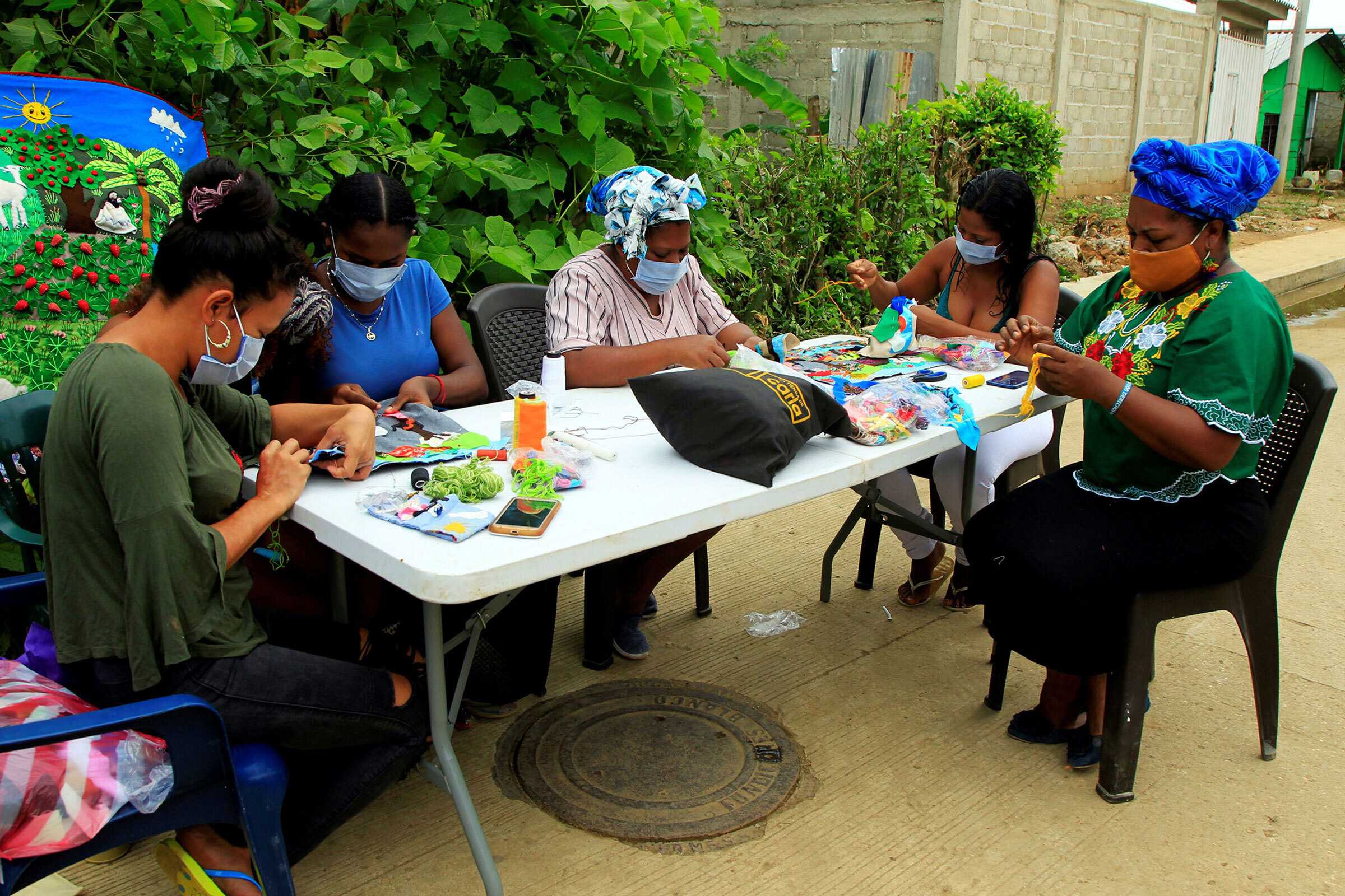 5 mampujan weavers work on weaving projects on a folding table outside while wearing mask.