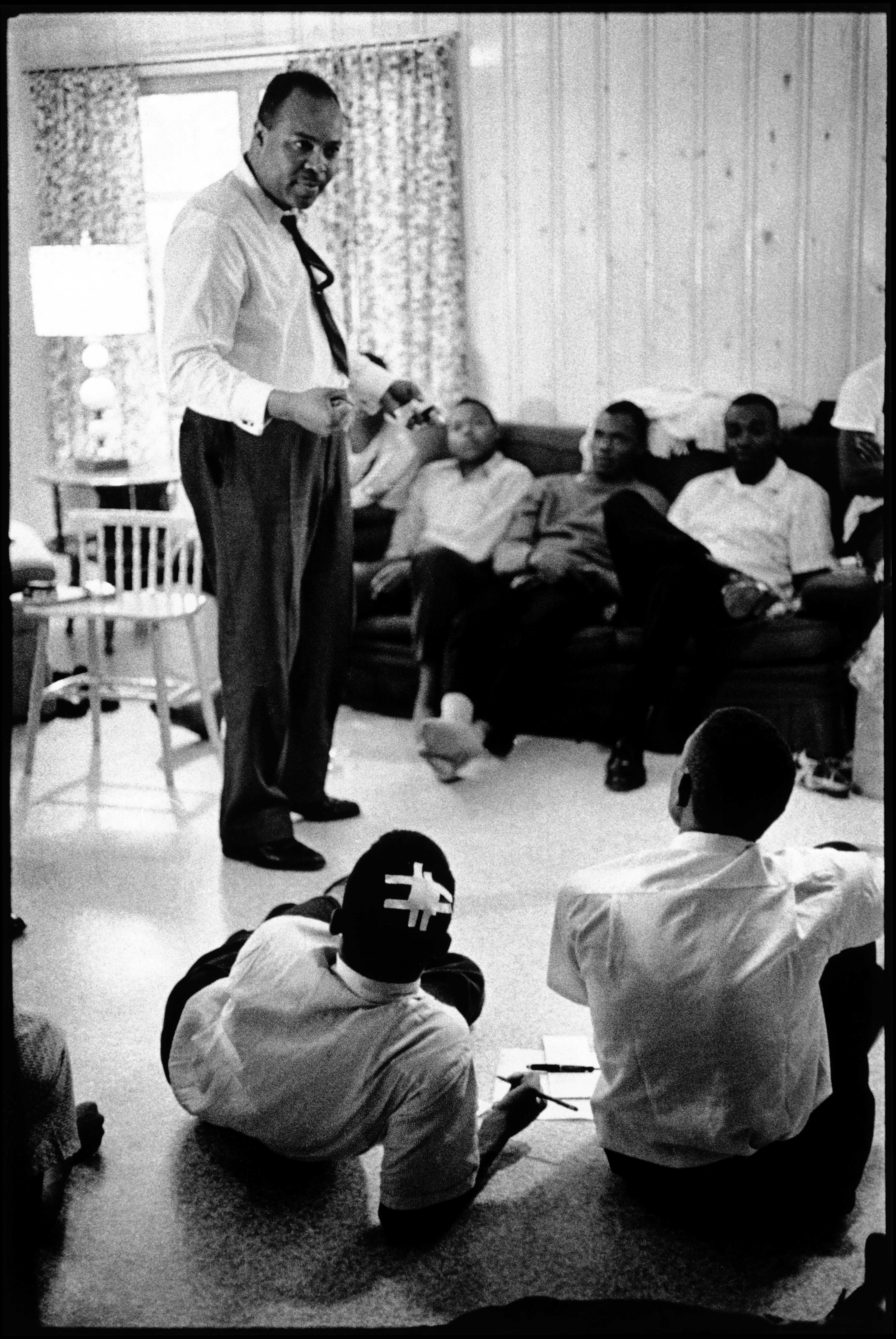 Black and white photograph of James Farmer speaking to a group of young men including John Lewis.