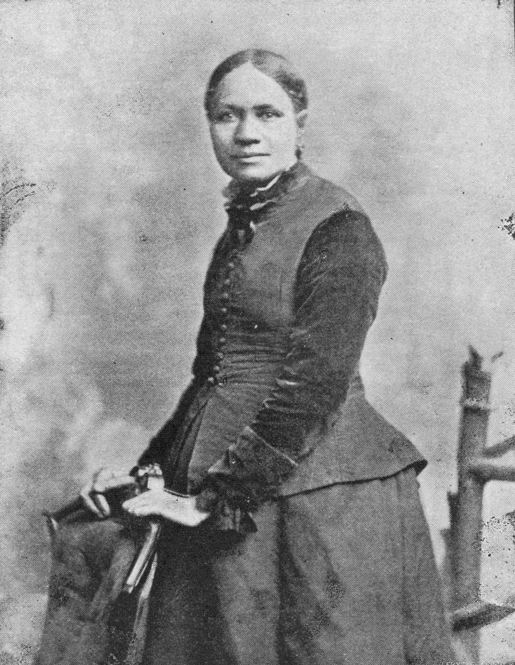 Black and white portrait of Black woman in three-quarter view with hands placed on the back of a chair.