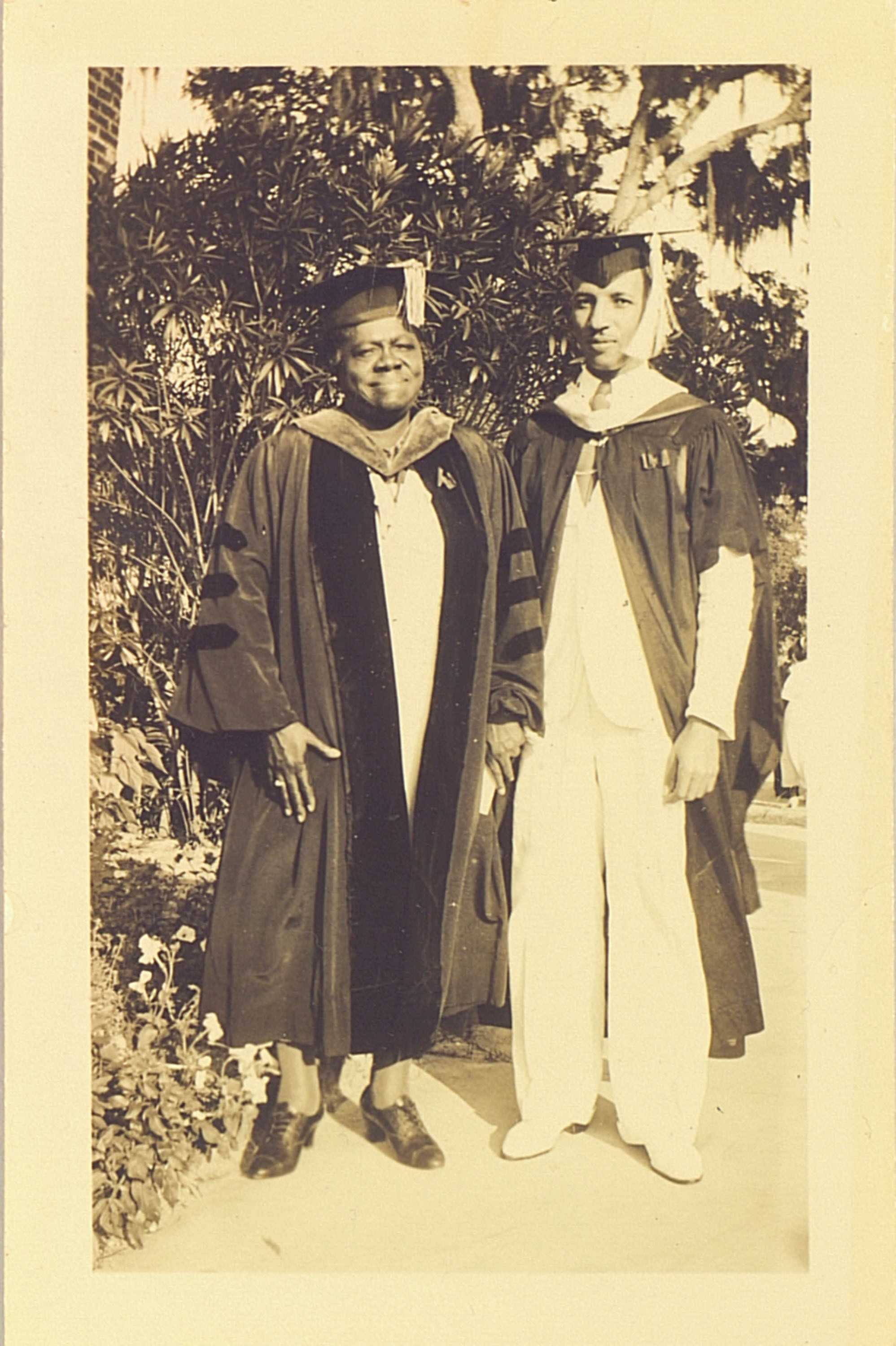 Black and white full lenght portrait of woman and man dressed in graduation dress.