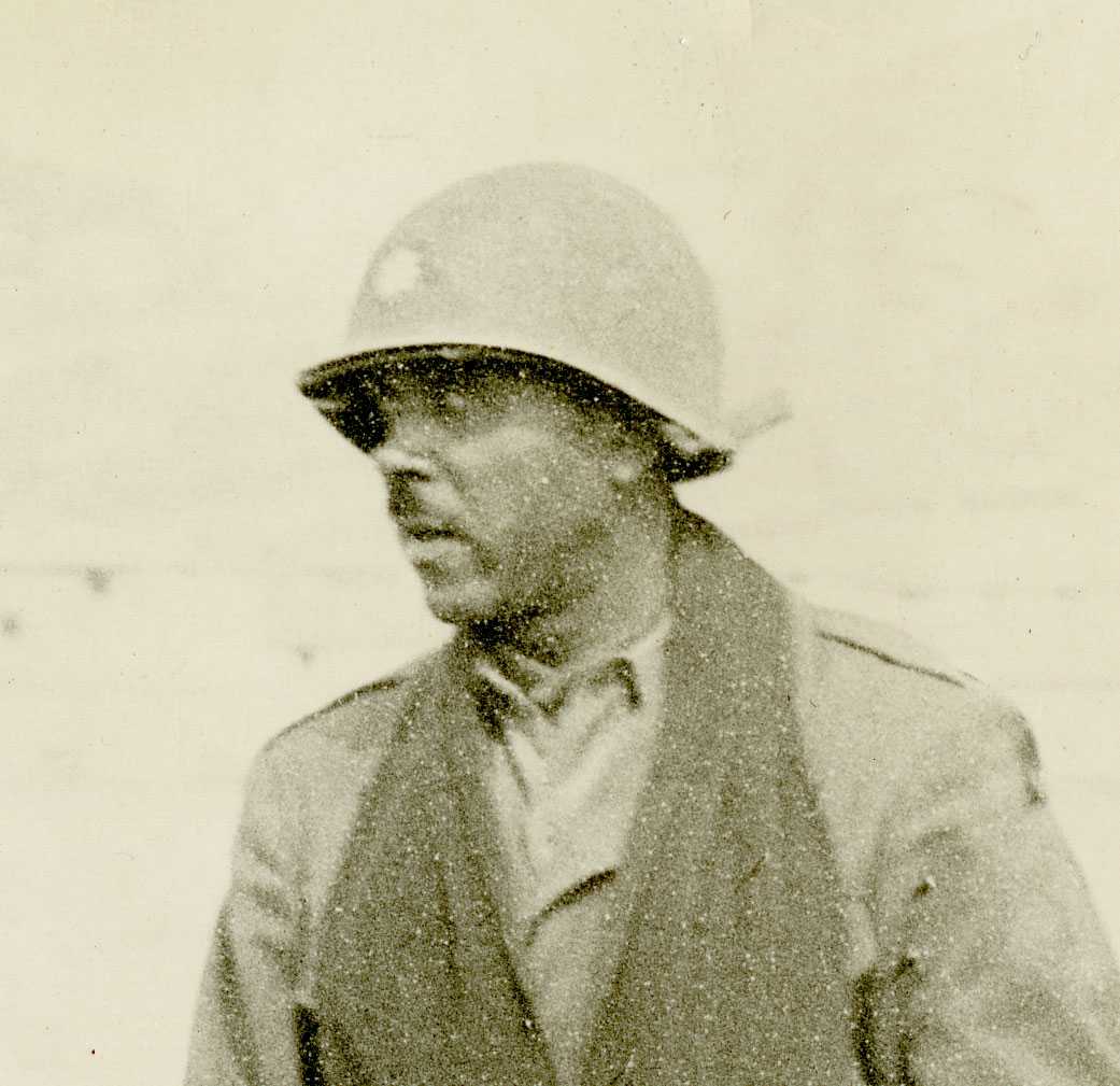 Black and white photograph of a man with head turned looking away from camera.  He is wearing a military hardhat and a uniform.