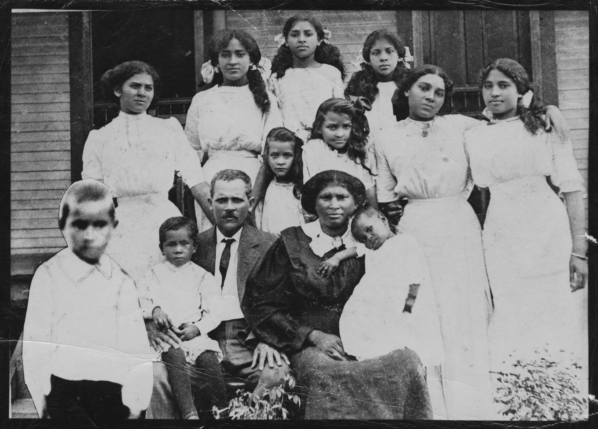 A family portrait with 11 children and their parents. The 6 teenaged daughters stand behind their parents in white dresses.