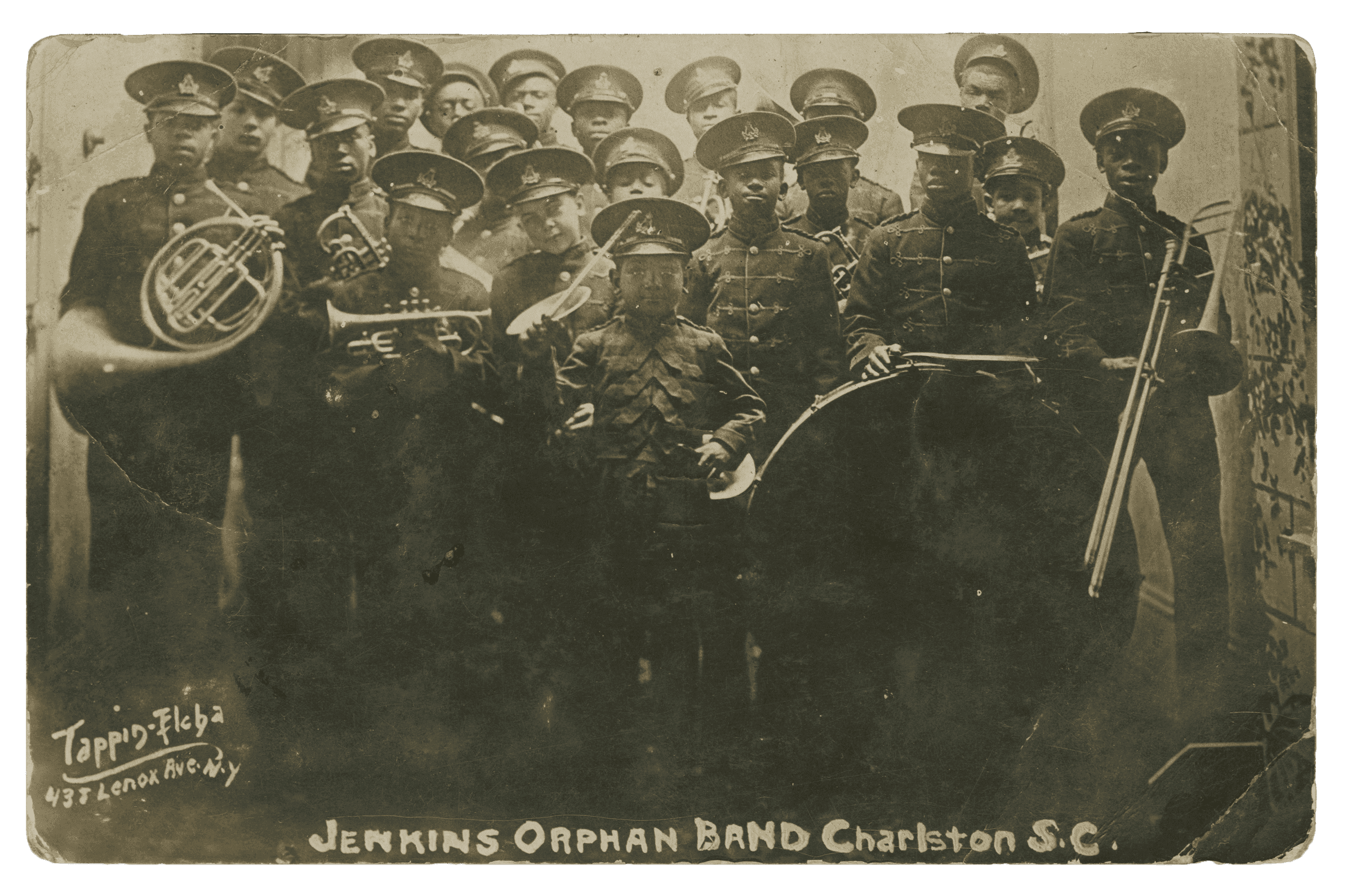 A black and white photograph postcard of twenty boys and young men in uniform stand in rows holding instruments. At the bottom is printed “JENKINS ORPHAN BAND Charleston S.C.”