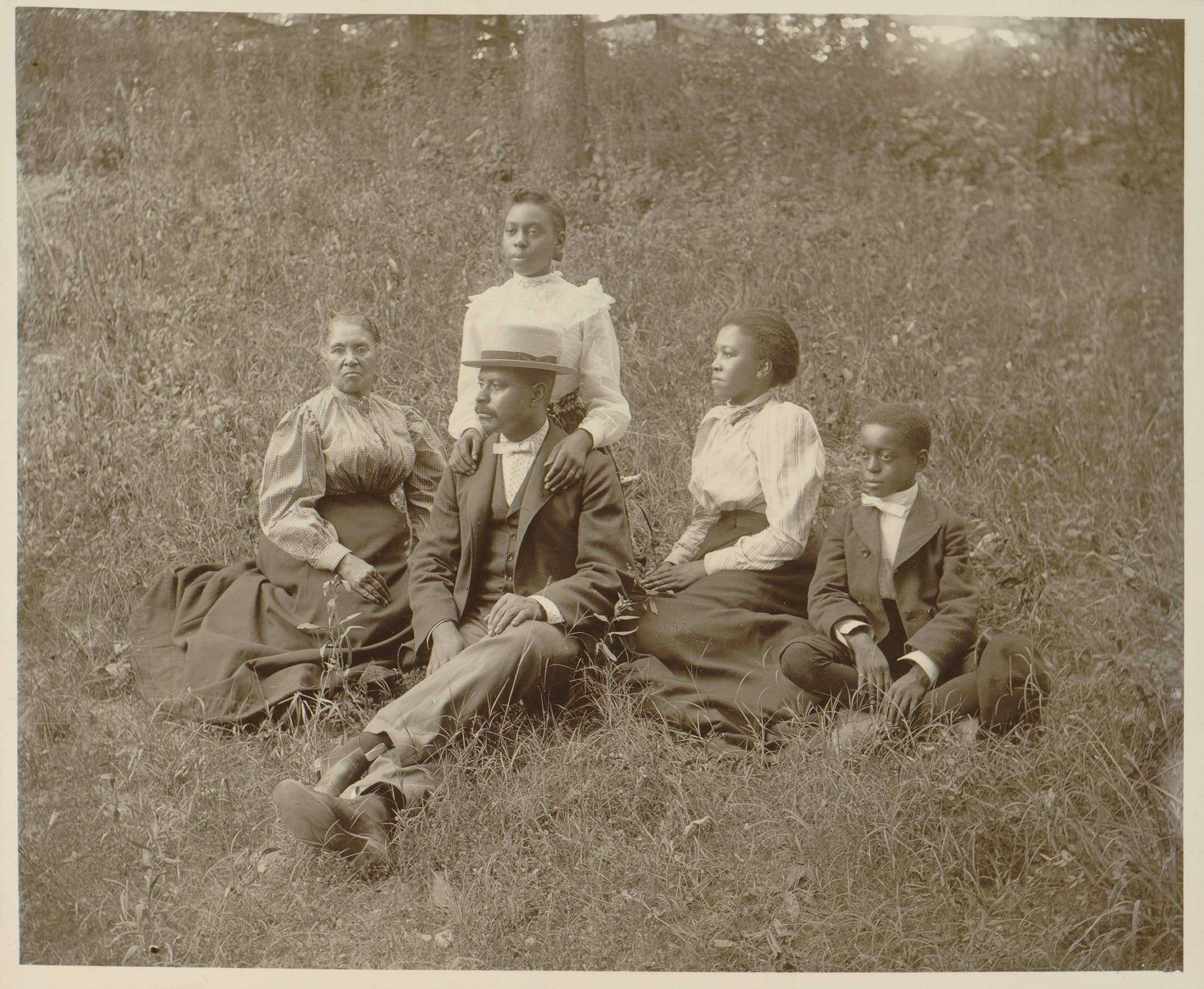 A sepia tone photo of a family. Mother and father are on the left, while their 3 children sit next to them.