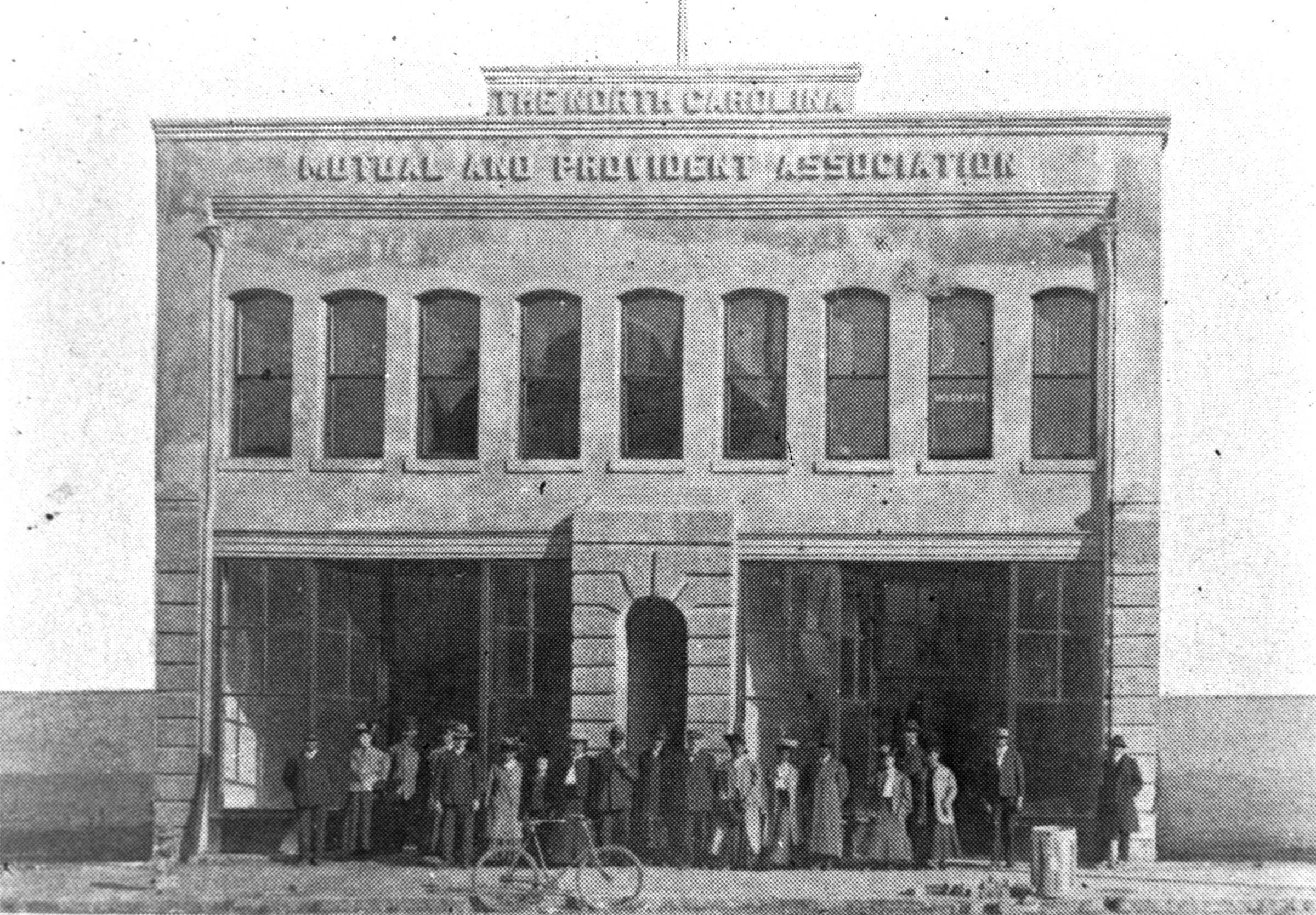 Black and white image of "THE NORTH CAROLINA / MUTUAL AND PROVIDENT ASSOCIATION." There are a line of unidentified people standing in front of the large stone building.