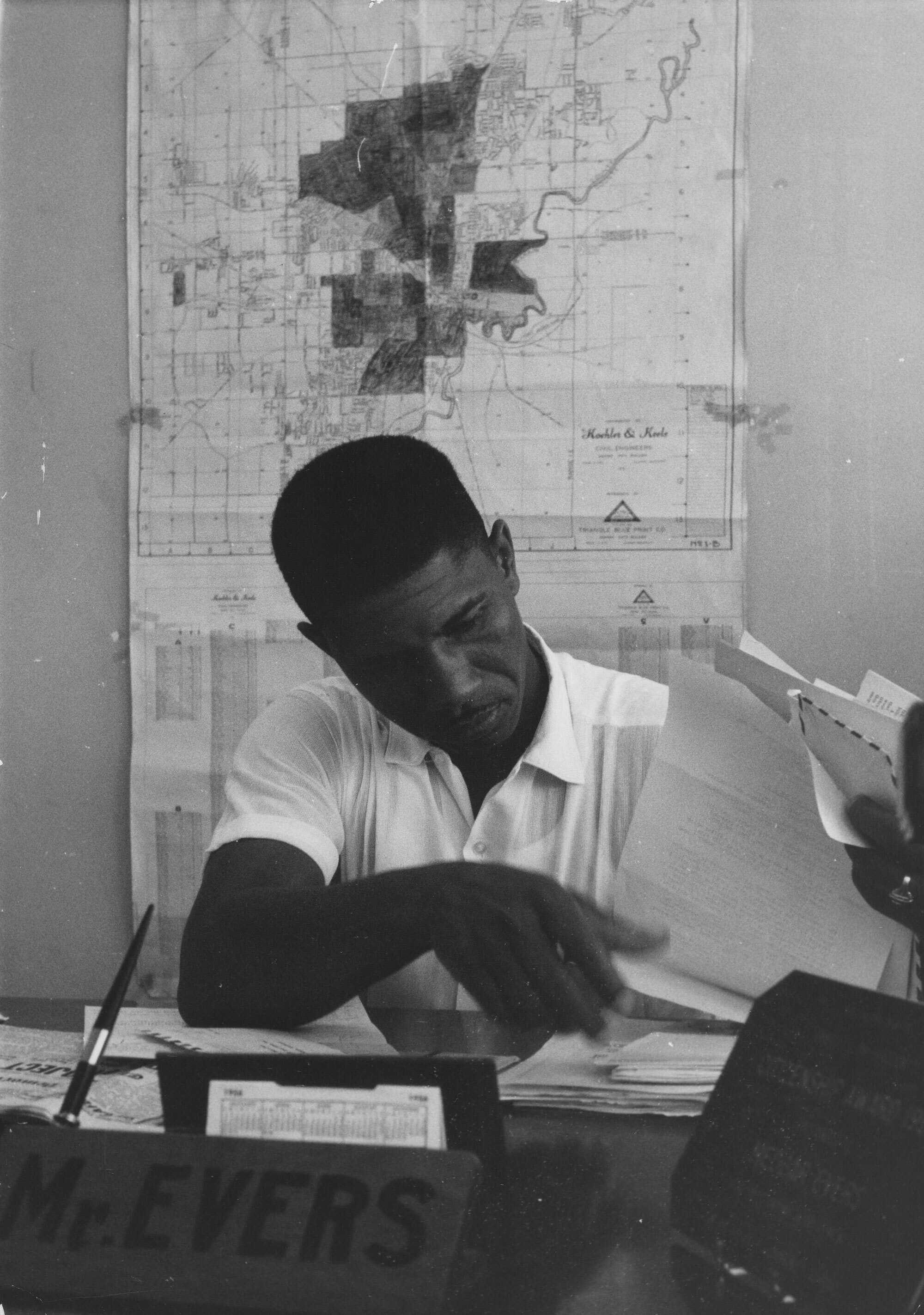 Black and white photograph of Medgar Evers seated at his desk.