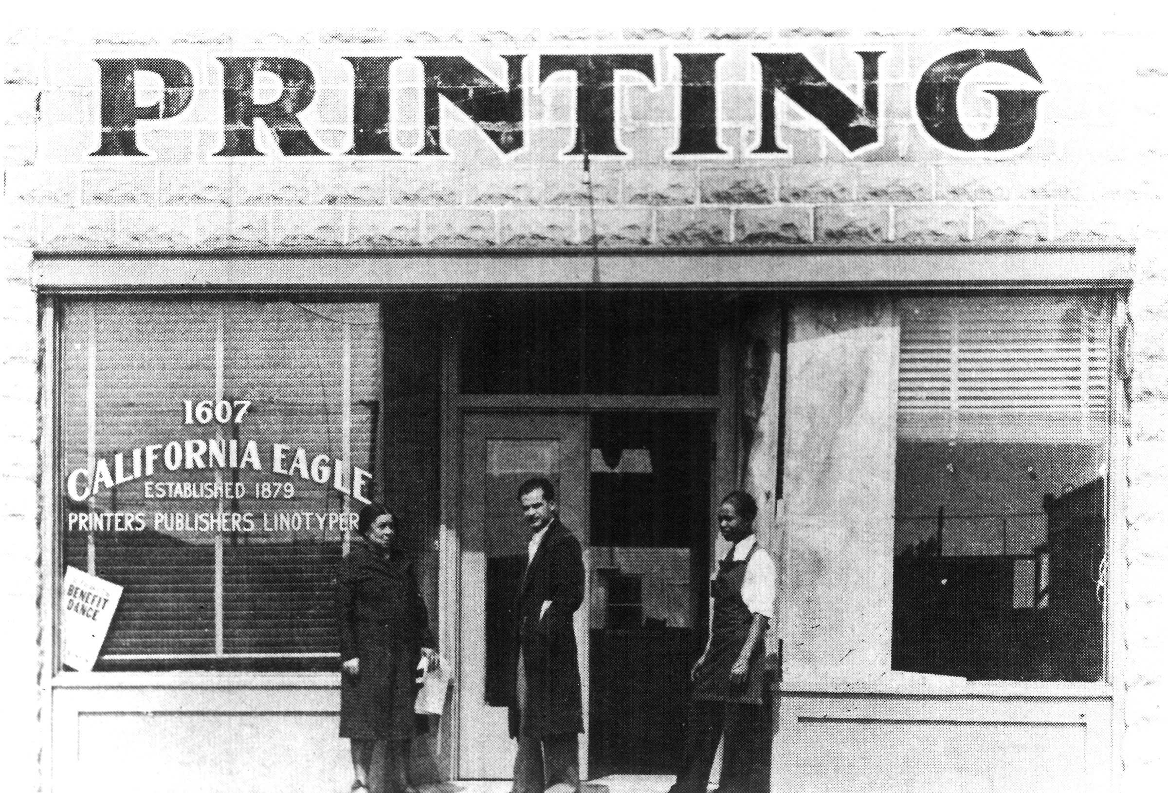 Black and white photograph of 3 people standing in front of a building marked 'PRINTING / 1607 / CALIFORNIA EAGLE / ESTABLISHED 1879 / PRINTERS PUBLISHERS LINOTYPE"