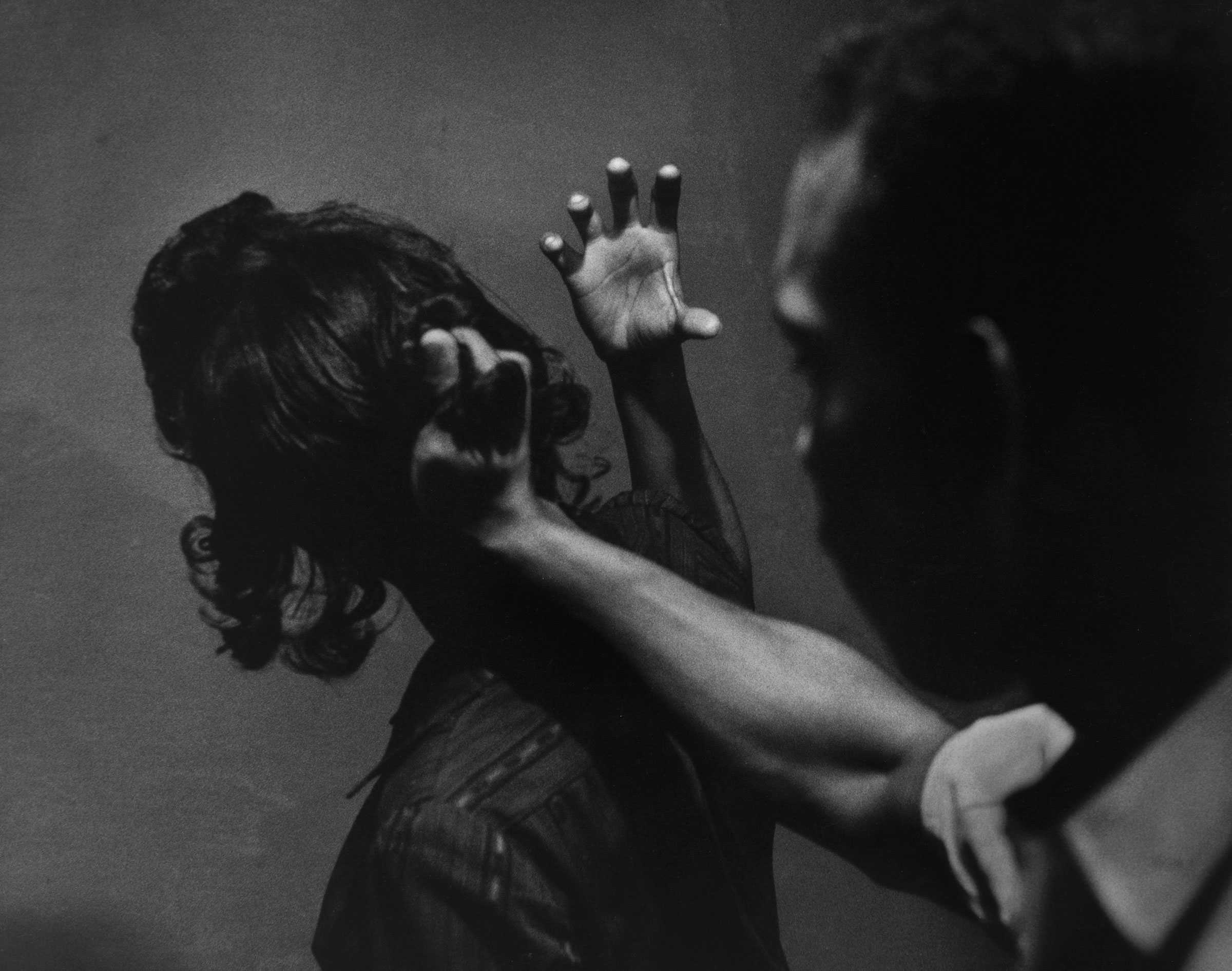 A black and white photograph of two a man grabbing a woman's hair from the back as part of Passive Resistance Training.