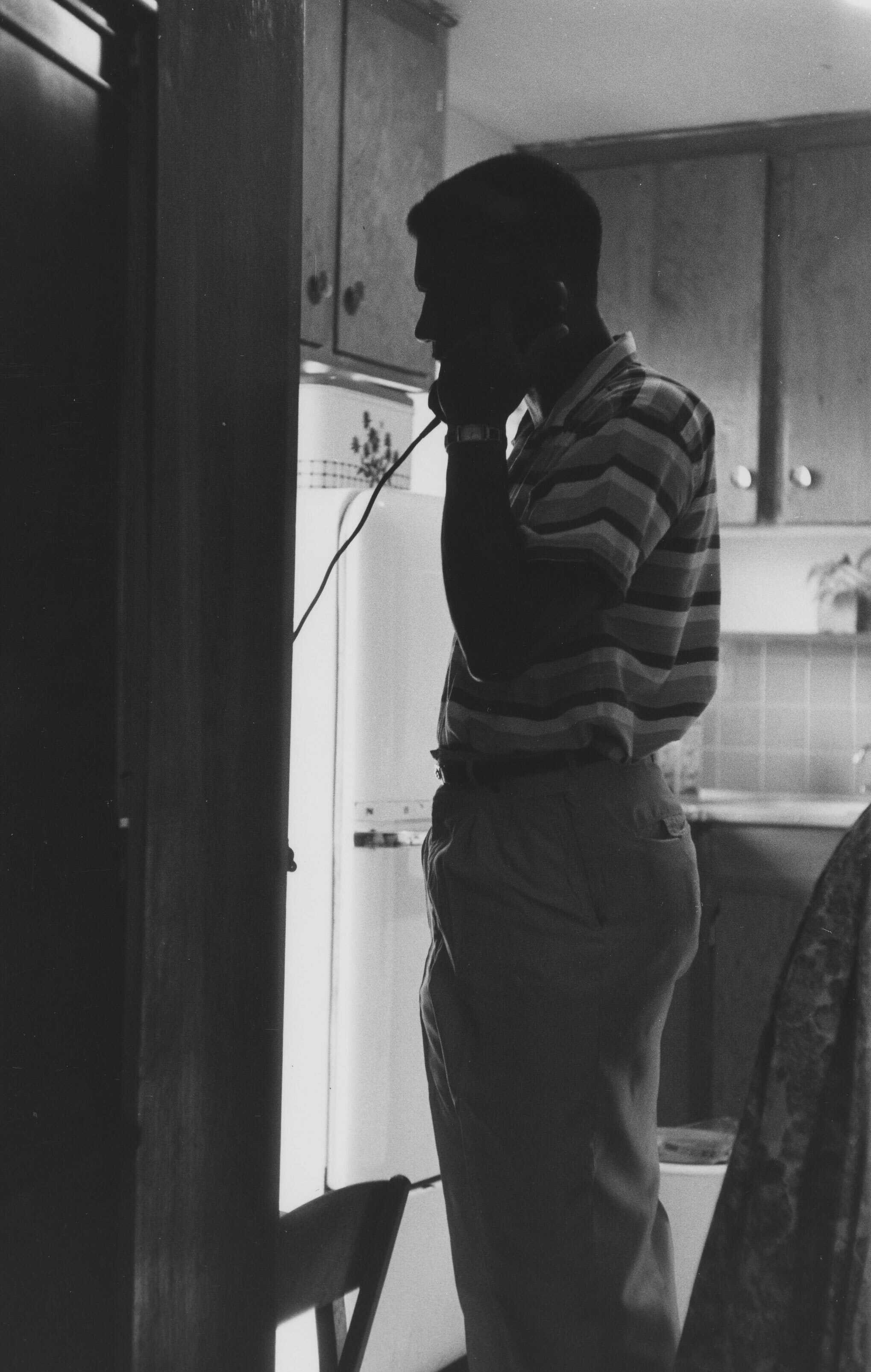 Black and white photograph of Medgar Evers standing in profile, talking on the phone.