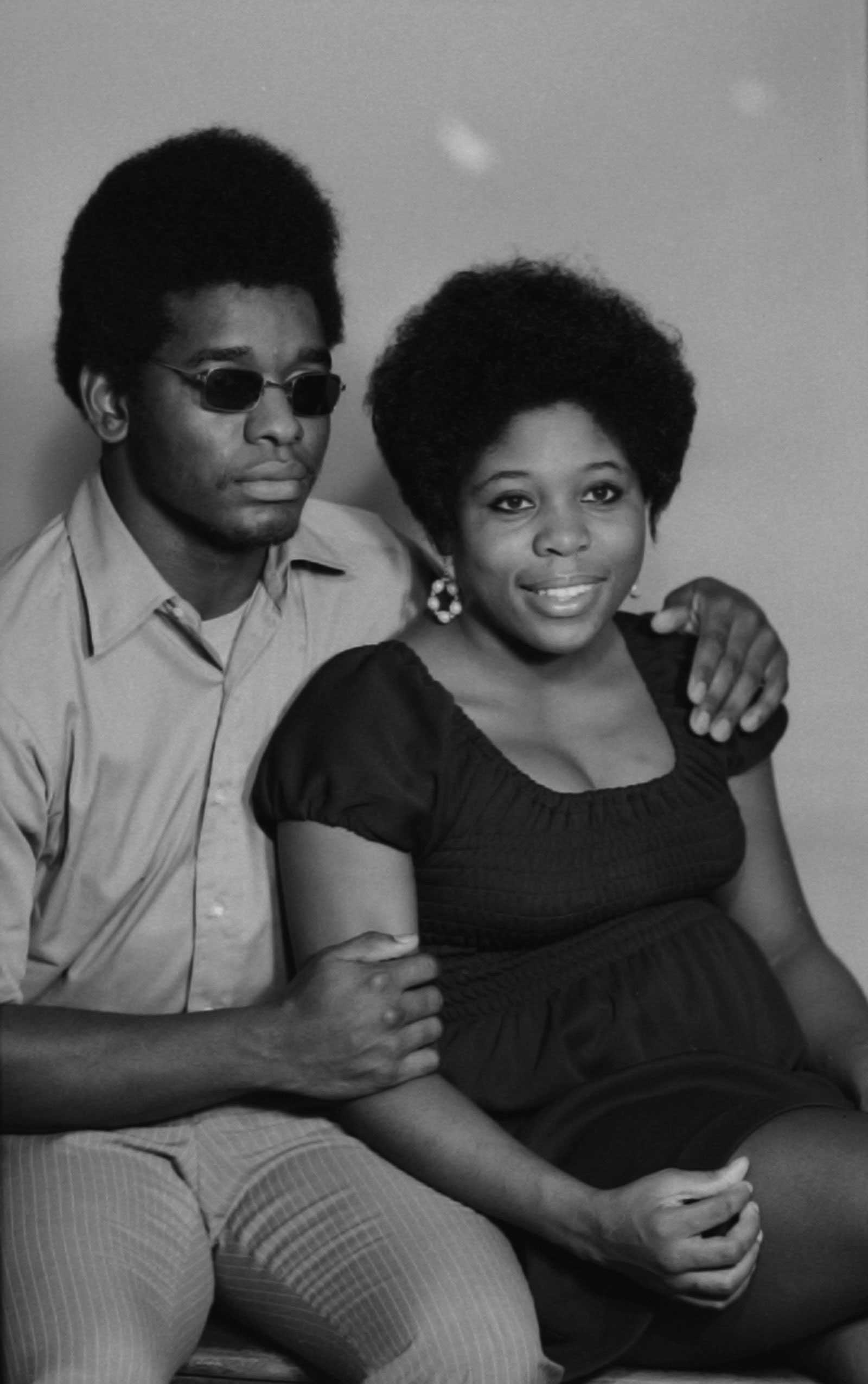 A black-and-white diptych of a couple sitting in a studio. He wears sunglasses, and she smiles in a dress.