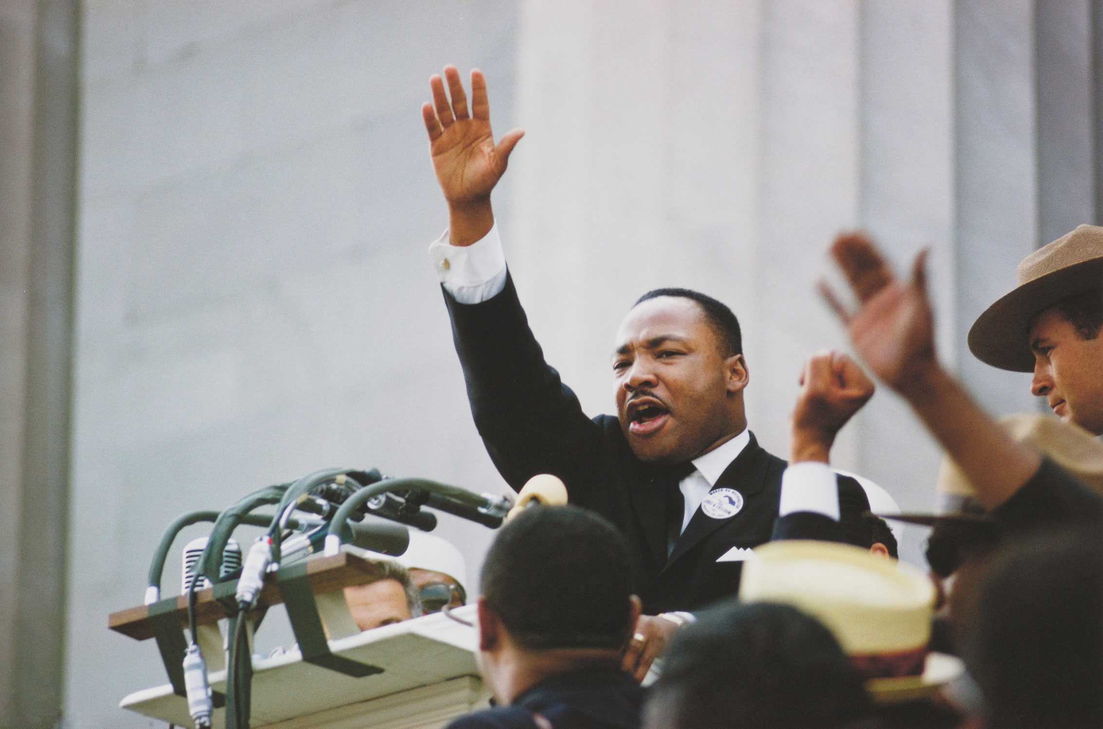 A color photograph of the 1963 March on Washington photo of Dr. Martin Luther King Jr. waving from a podium with microphones.