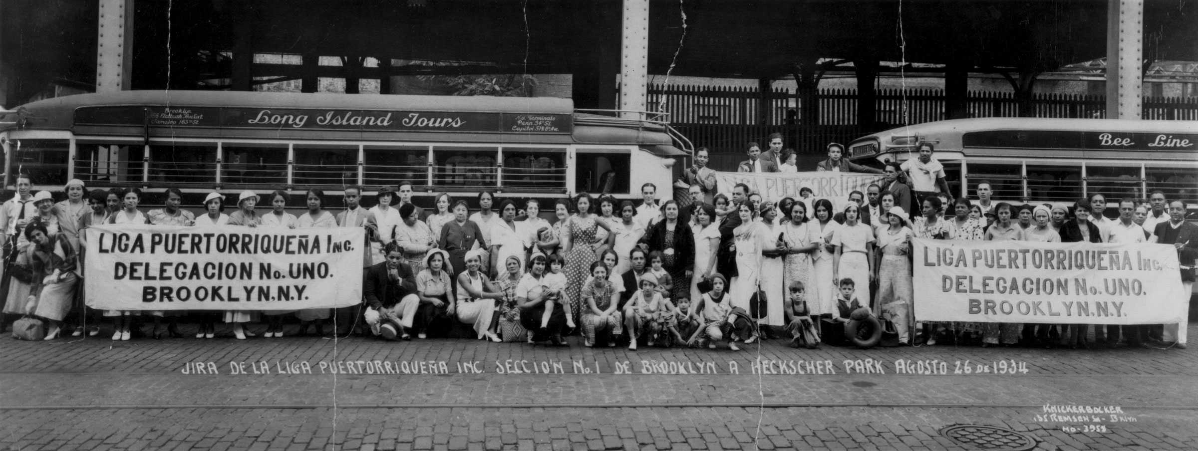 Photograph of a group of people standing in front of a bus. They are holding a sign.