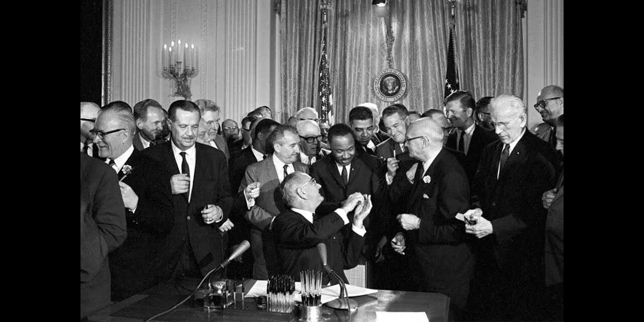 President Lyndon B. Johnson signs the 1964 Civil Rights Act as Martin Luther King stands behind him.