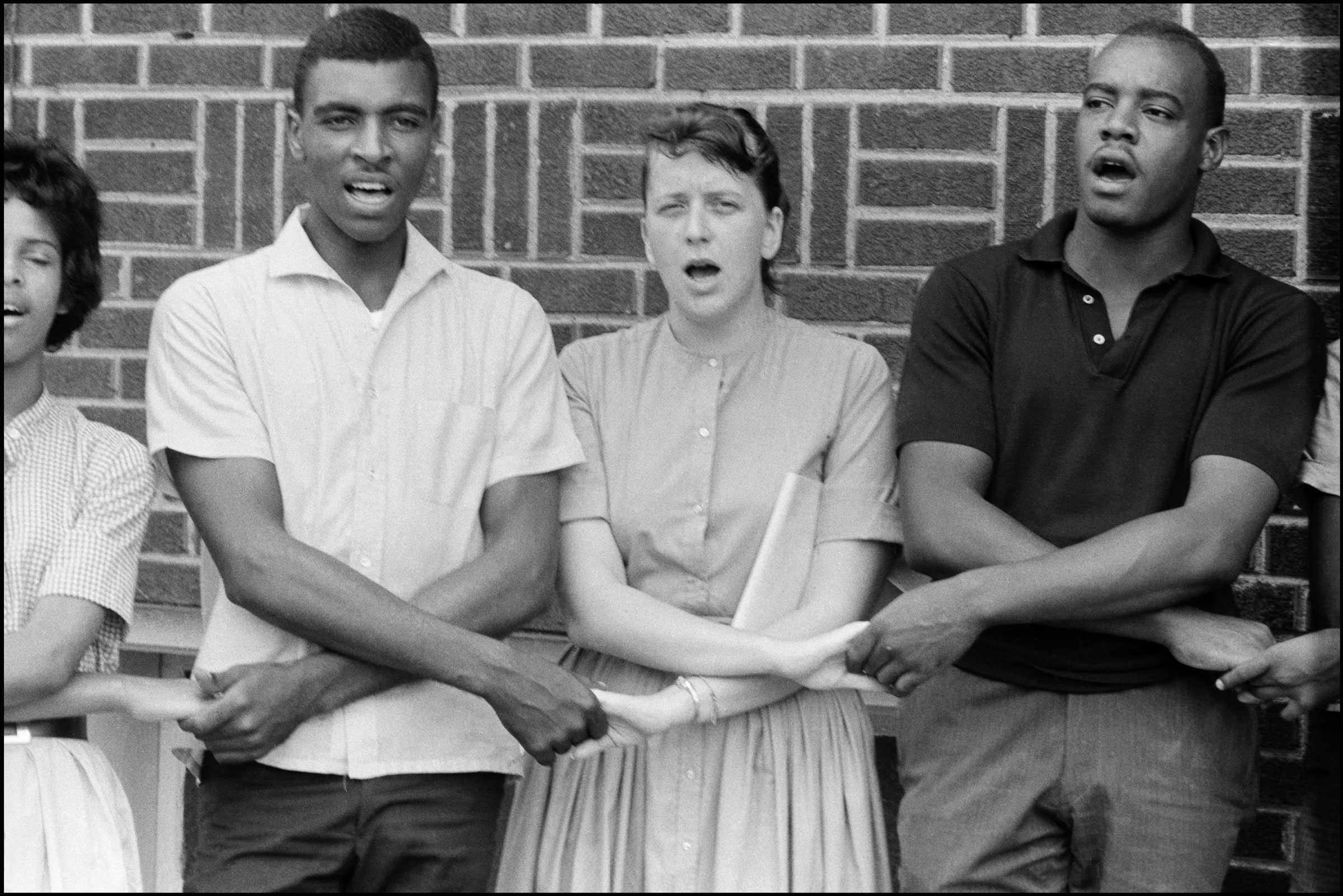 A black and white photo of Chico Neblett and Selyn McCollum demonstrating outside. They are holding hands and chanting.