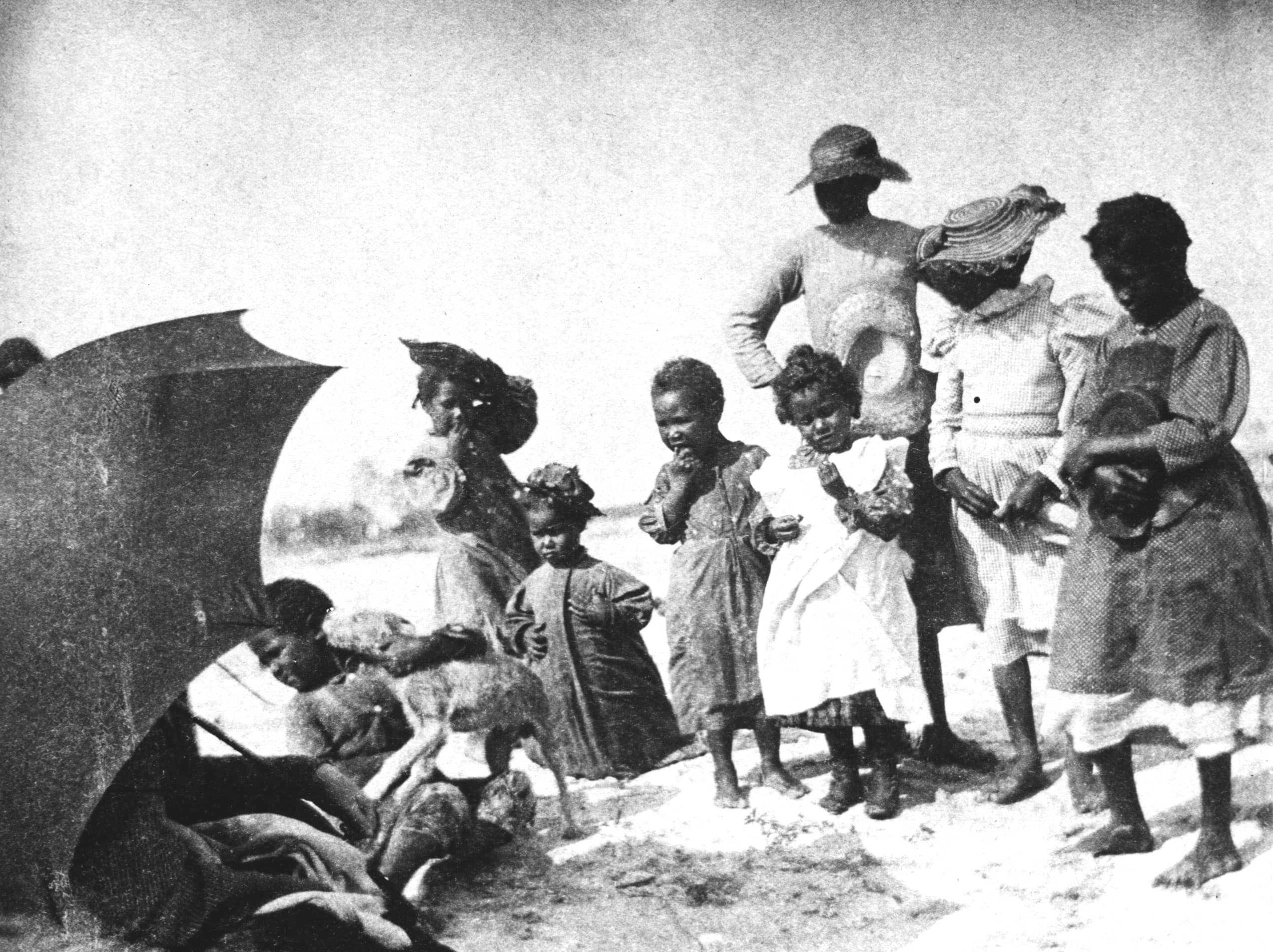 A blurry black and white photo of a children, ranging from toddler to preteen, stand near an umbrella with a dog.