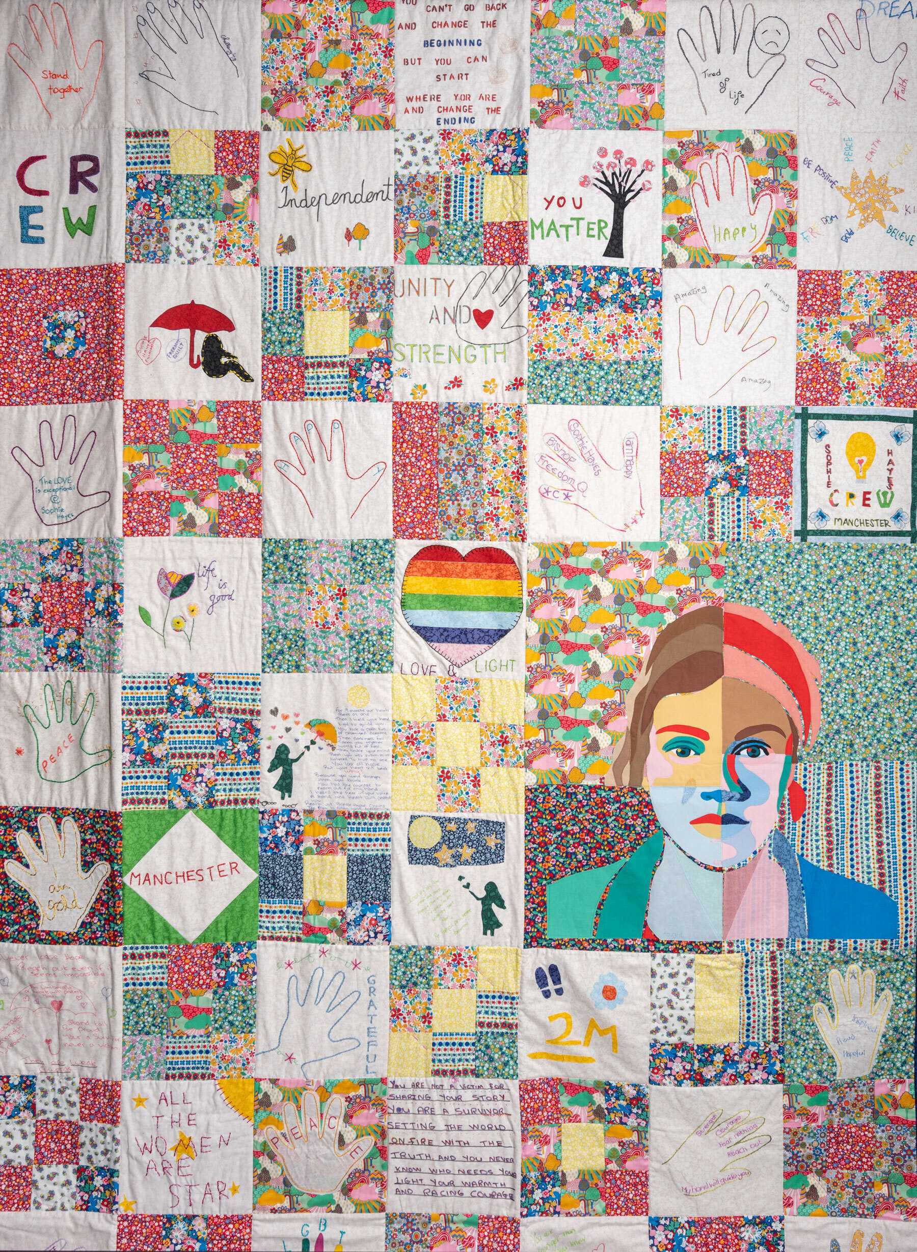 A colorful quilt with many squares with different patterns and designs. A portrait of a woman is made up 4 different colored squares.