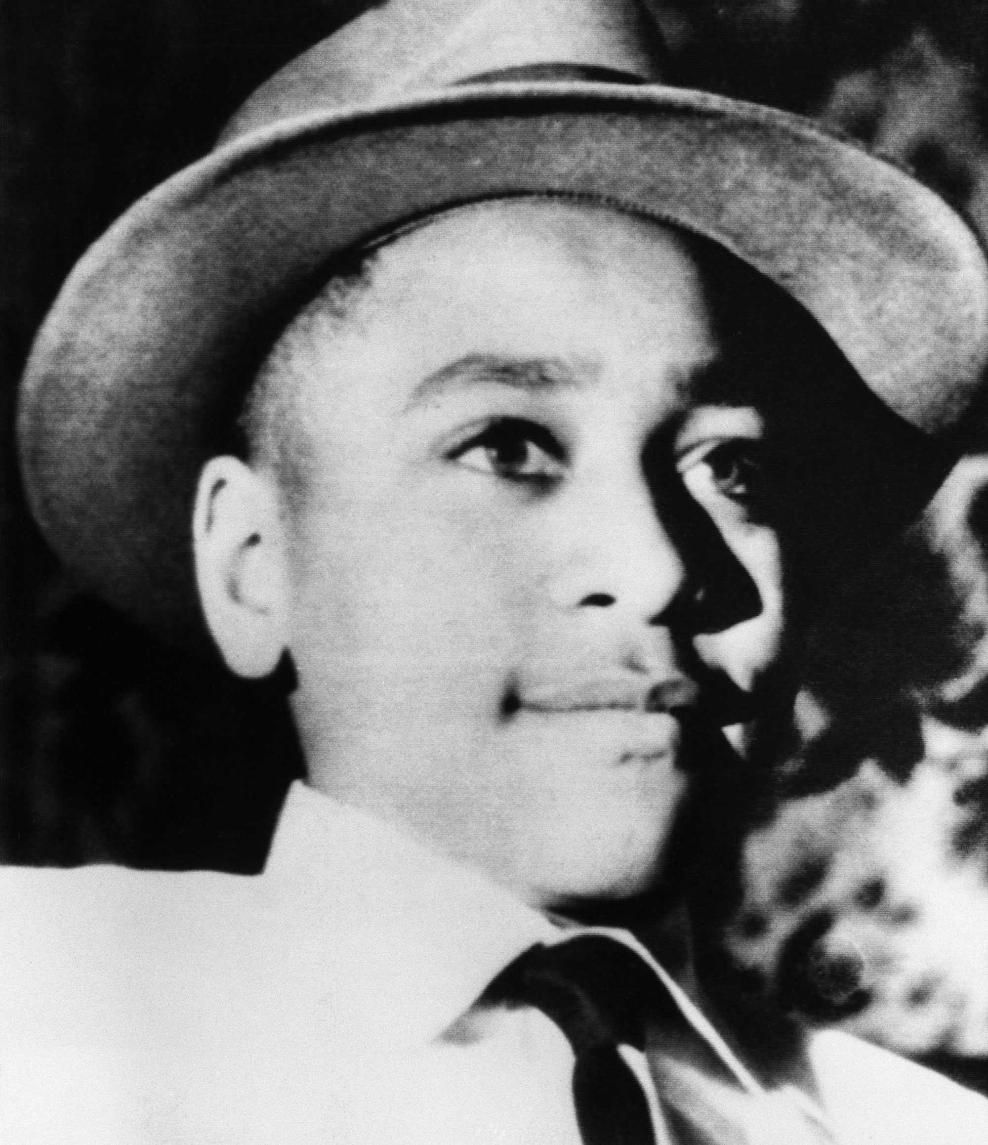 A close up, black and white portrait of young Emmett Till. He wears a hat and looks off camera.