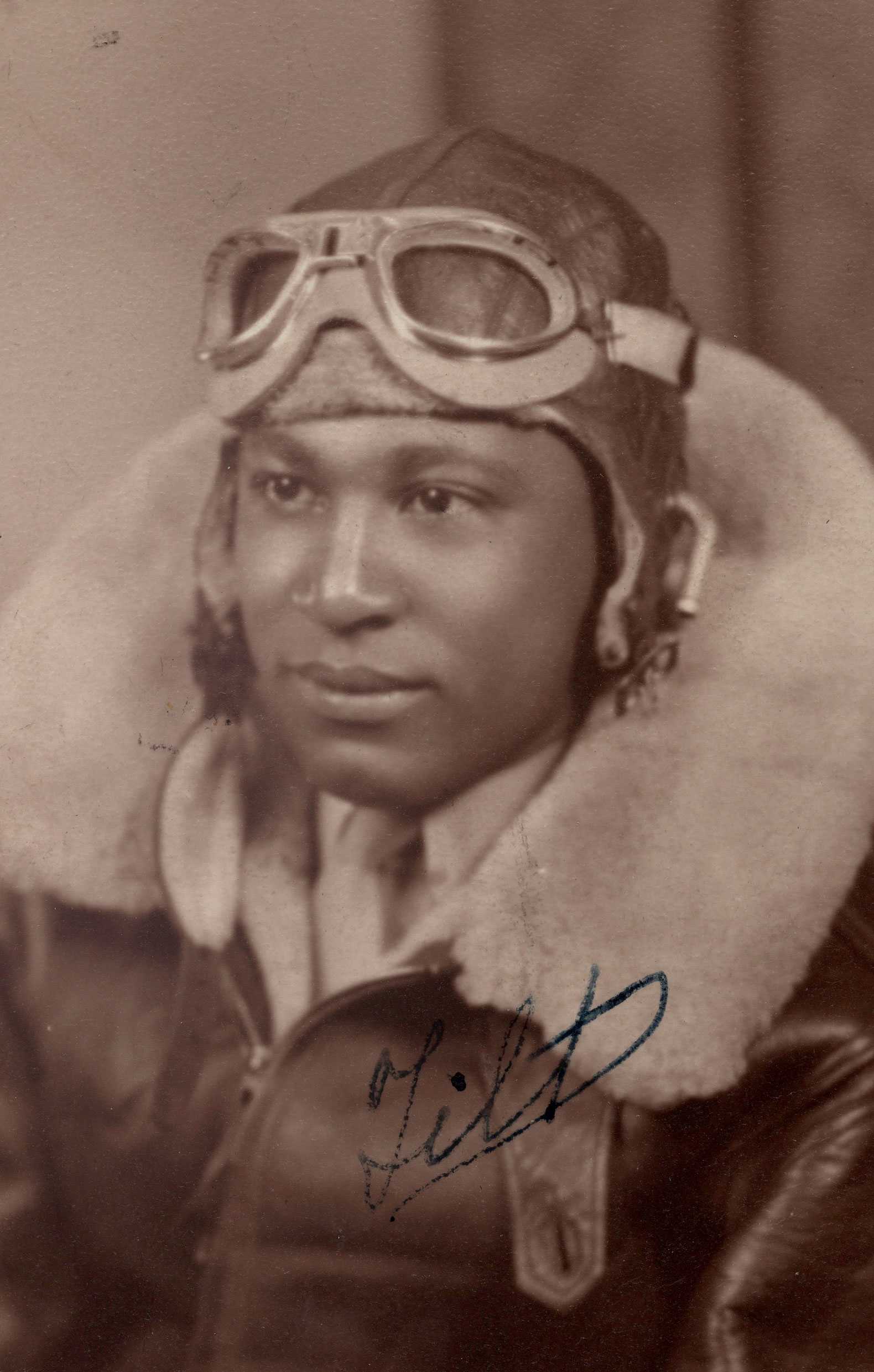 A black-and-white gelatin silver print of a Tuskegee Airman in aviation gear. He faces left, wearing an A-11 helmet, 6530 goggles, and a jacket with a fur collar.