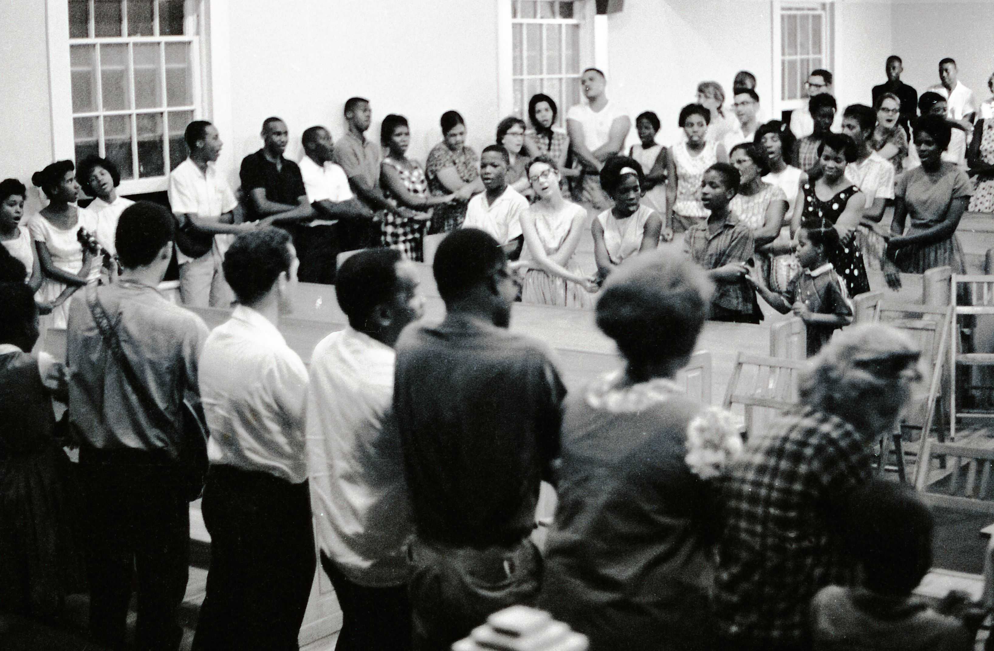 Black and white photograph of large group of students interlinked singing We Shall Overcome."