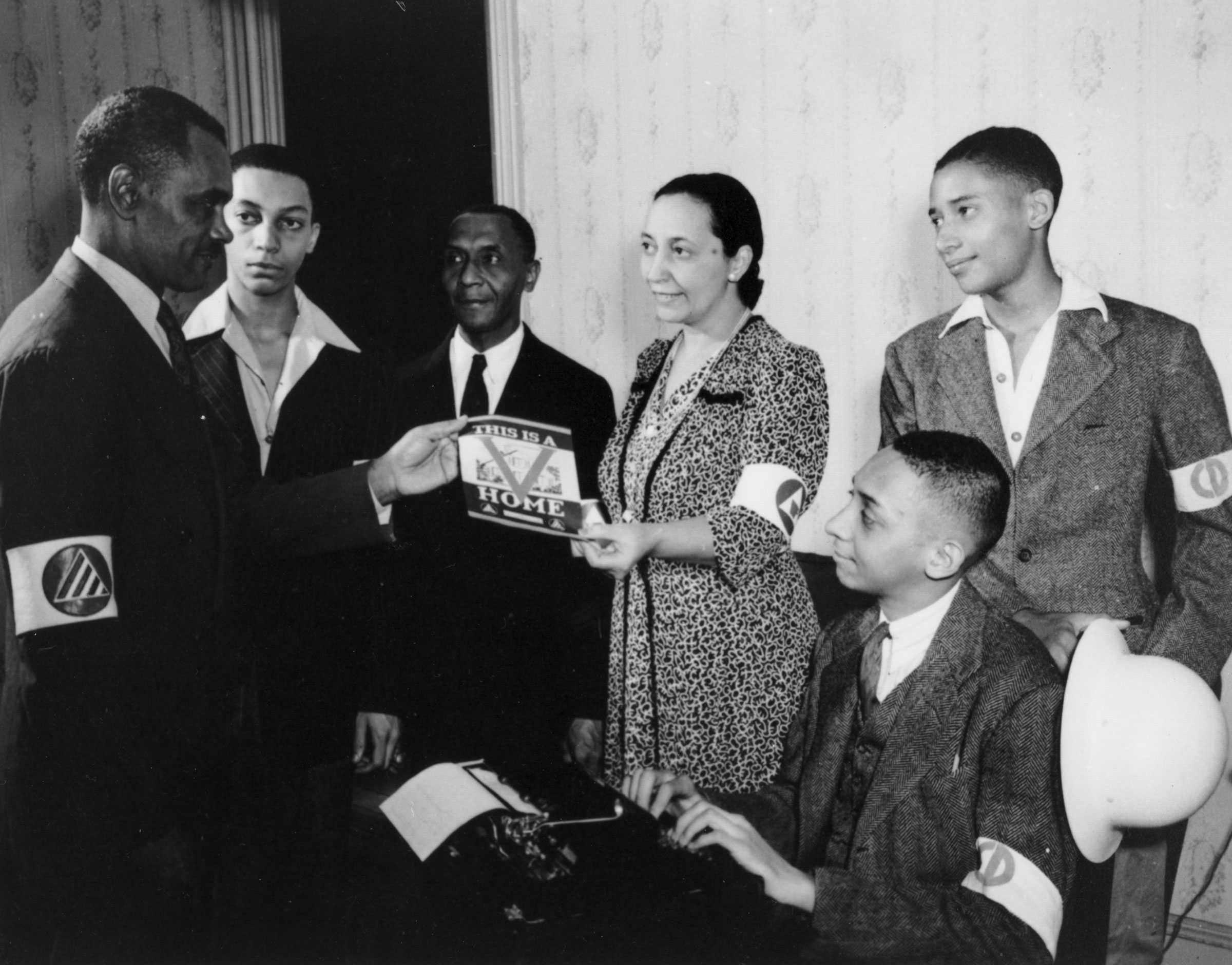 Black and white photograph showing a group of African Americans displaying a publication "THIS IS A V HOME."