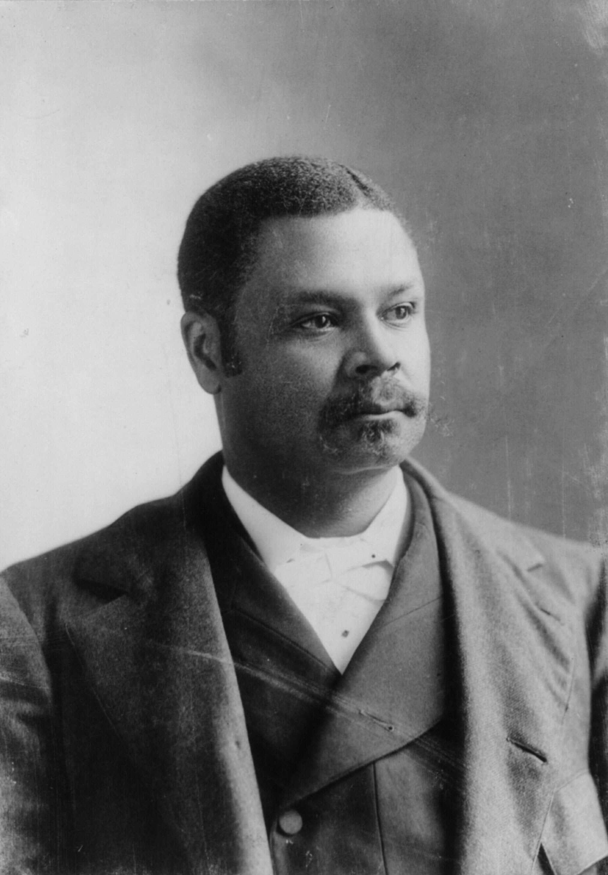 A worn black and white photo of George H. White. He is looking off camera in a suit.
