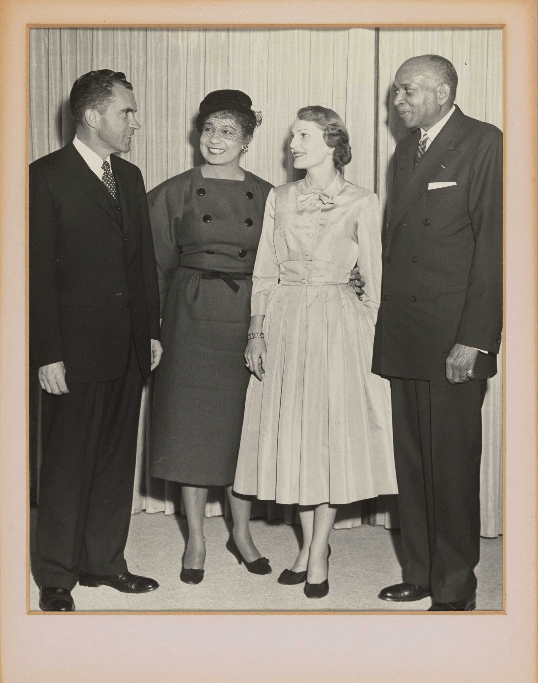 Black and white group portrait of 2 men and 2 women. The women are dressed in drssers while the men are in suits.