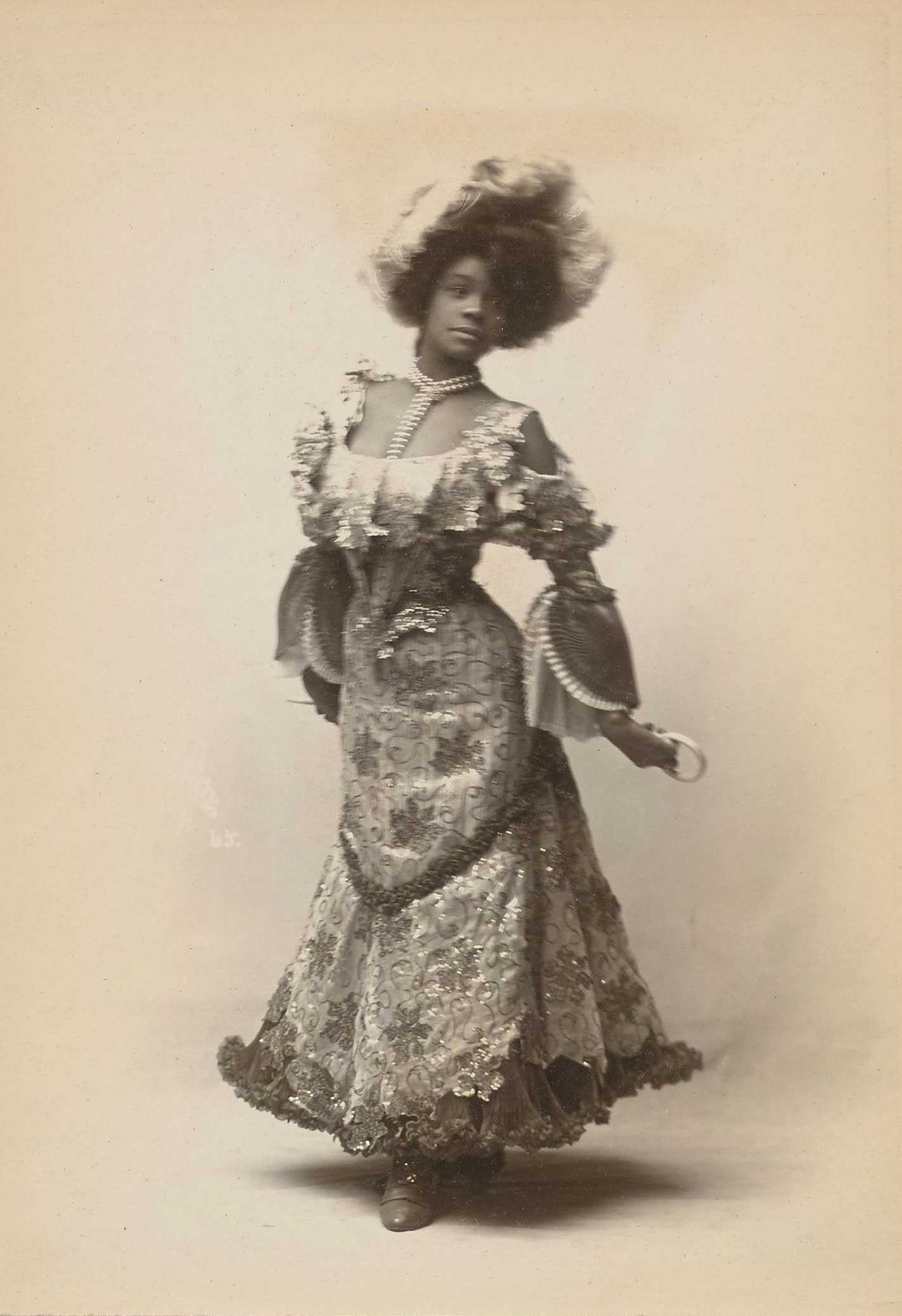 Black and white photograph of young Black woman wearing decorative dress, pearls and flowers in her hair.