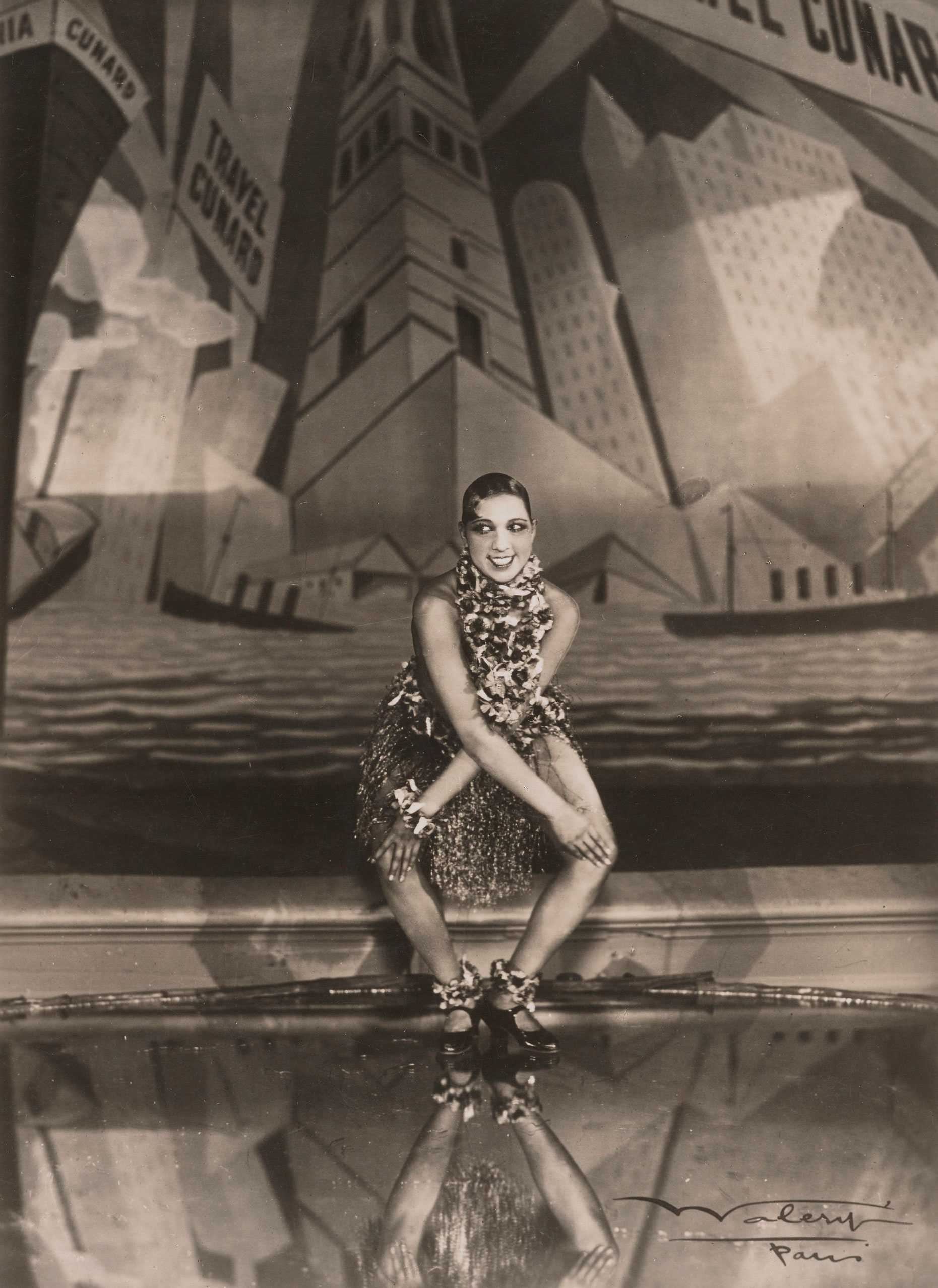 A black and white photo of Josephine Baker doing the Charleston centered stage in front of an art deco style backdrop.