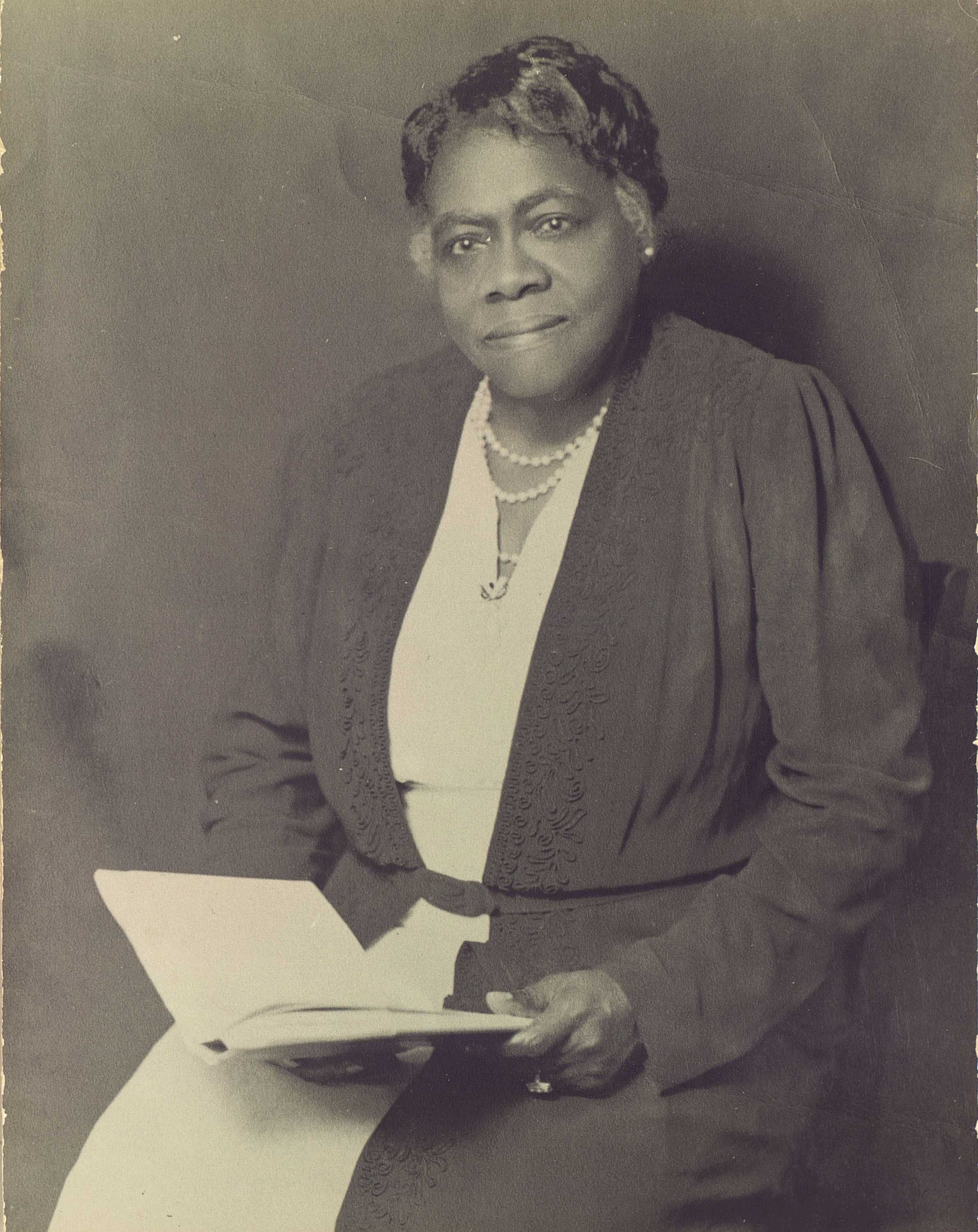 Black and white portrait photograph of women seated, holding a book open in her hands.