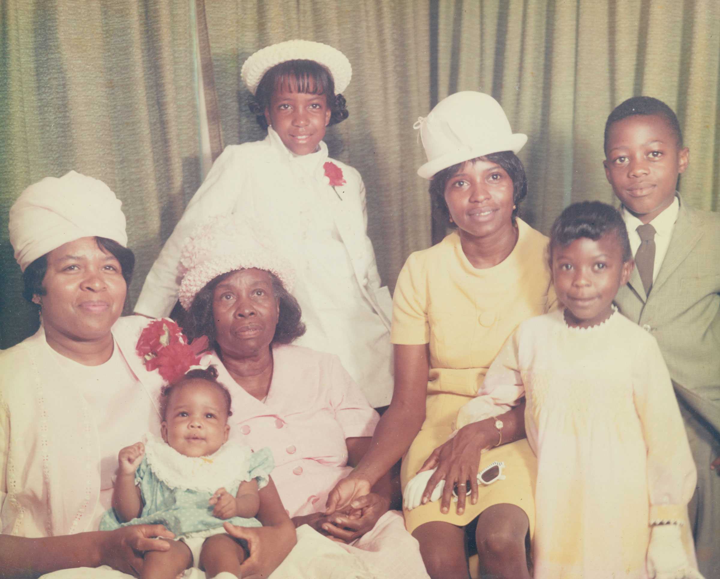 A color family portrait with three women, two girls, one boy, and a baby, all dressed in formal attire.