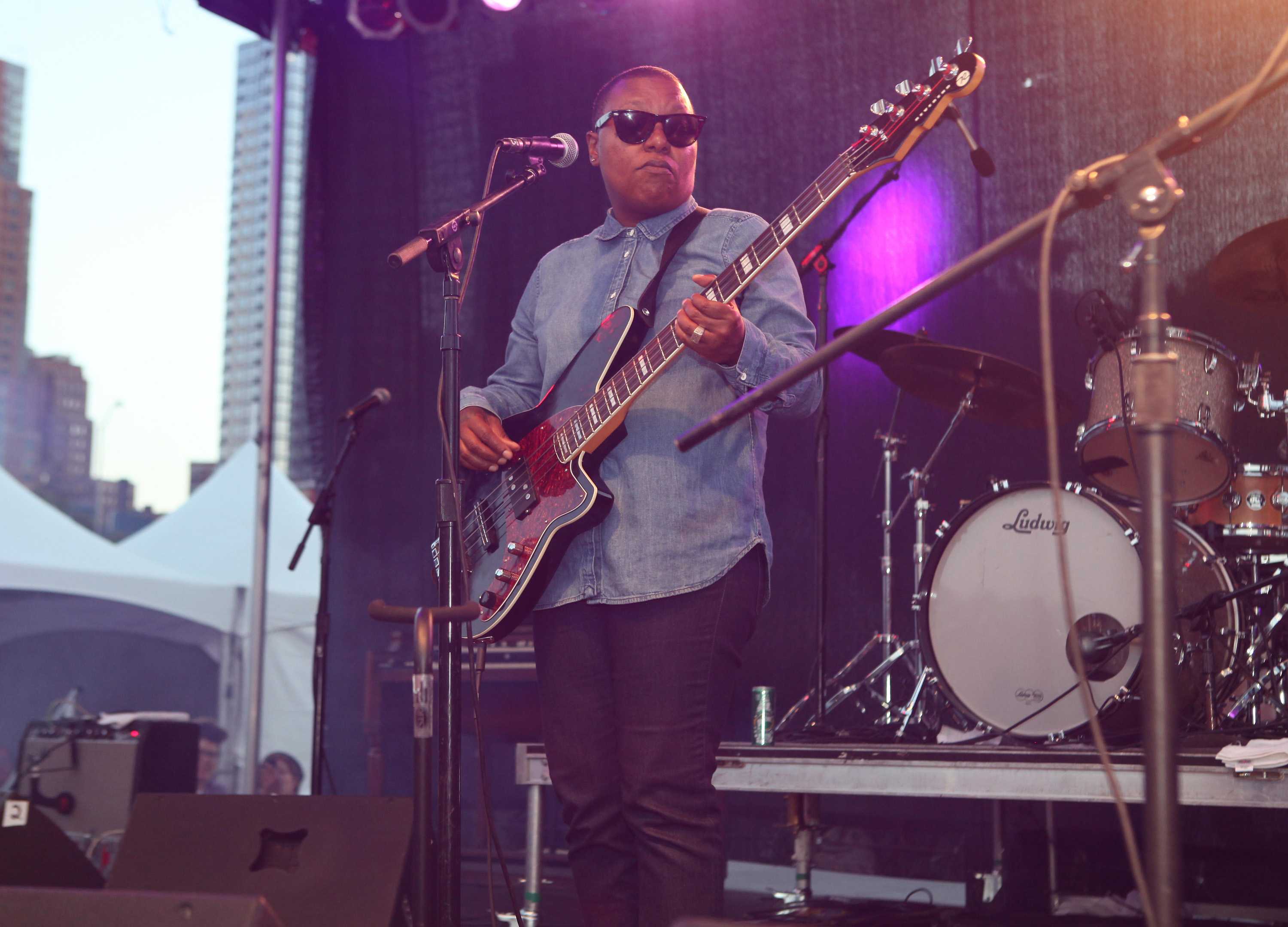 Meshell Ndegeocello playing the bass on stage with a microphone stand in front of him.