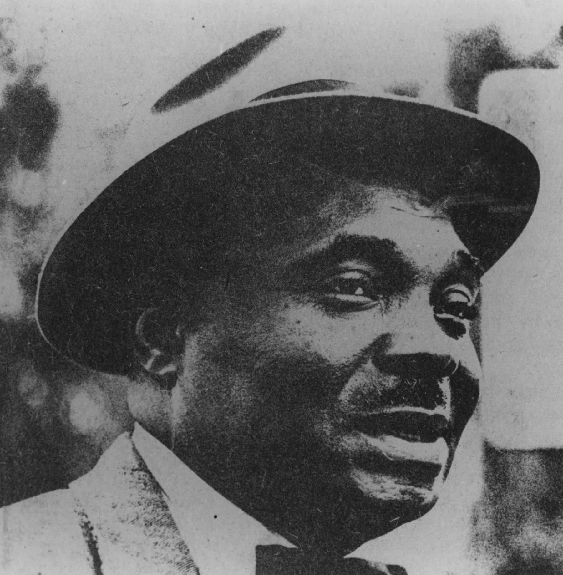 A close up slightly grainy, black and white photograph of Esau Jenkins. He is wearing a hat and looking off camera.