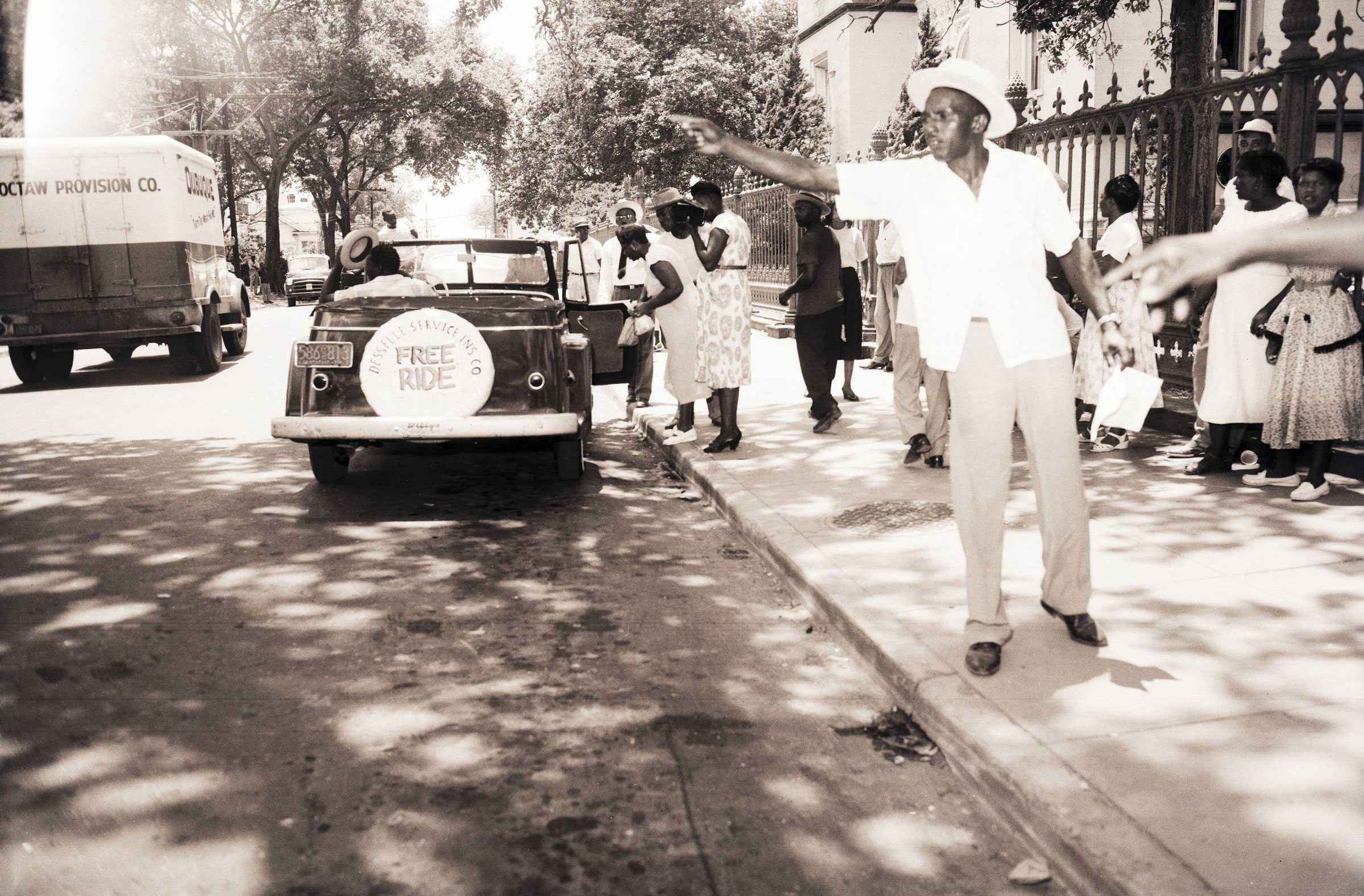 A black and white photograph of boycotters waiting on the streets get a carpool. One man directs a car to park.